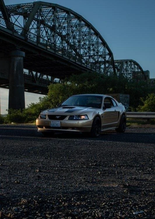 A silver sports car parked near a bridge under a darkening sky with greenery around.