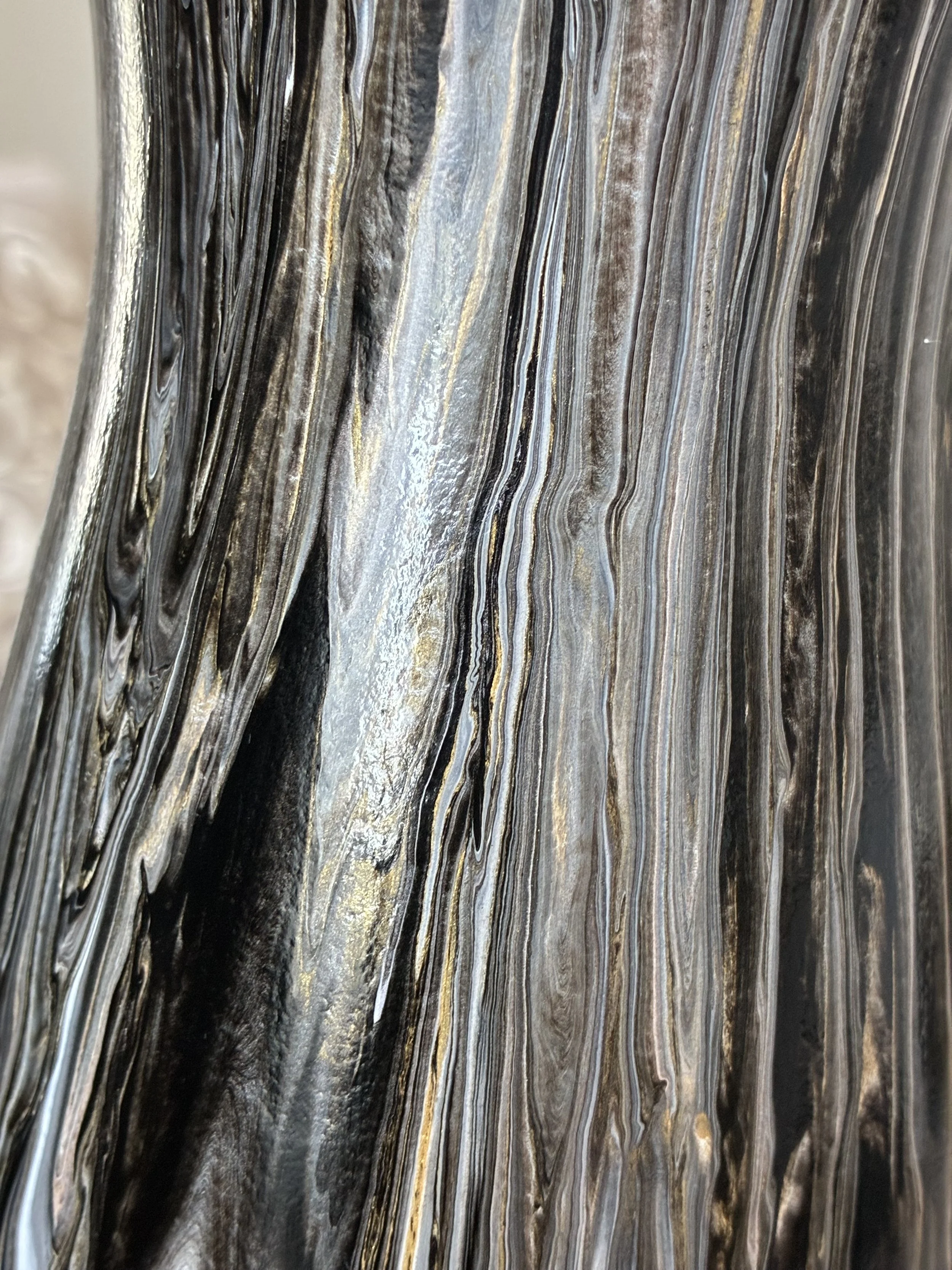 Close-up detail of a black, charcoal, silver, and bronze marbled vase featuring flowing mineral-inspired veining and metallic accents.