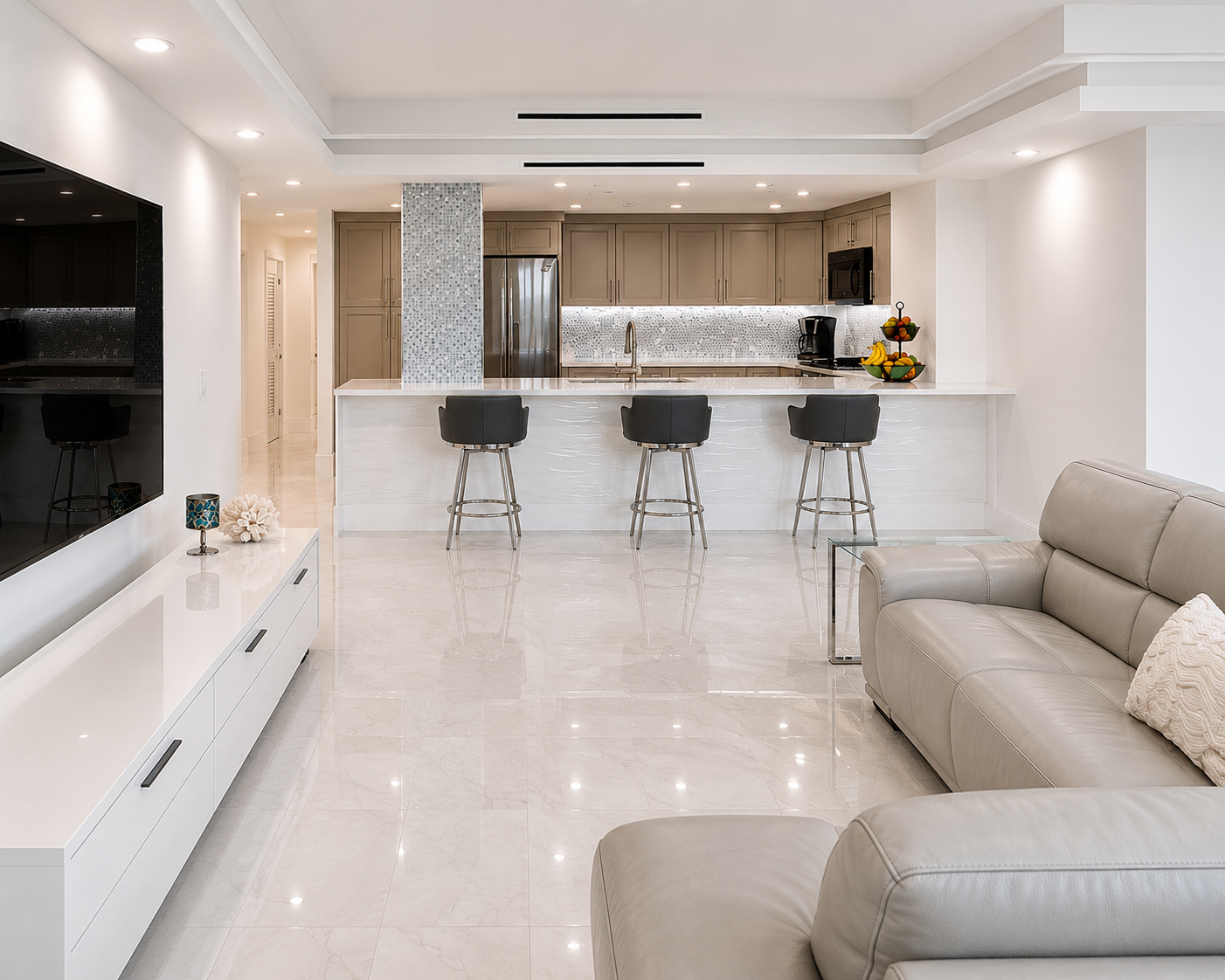 Modern open-concept living room and kitchen with beige leather sofa, white TV console, black bar stools at kitchen island, stainless steel appliances, and minimal decor.