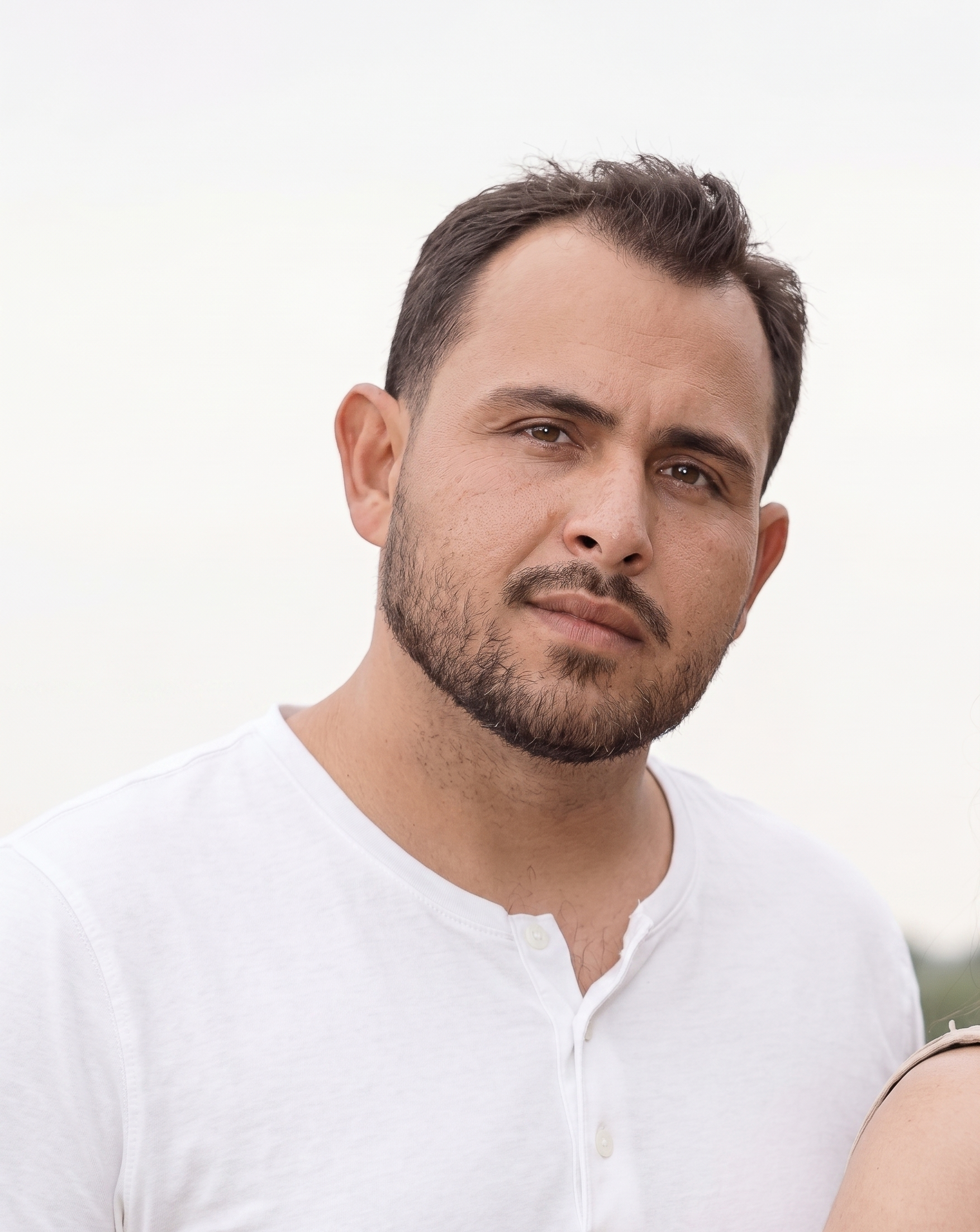 Close-up of a man's face and upper torso, wearing a white button-up shirt, against a plain white background.