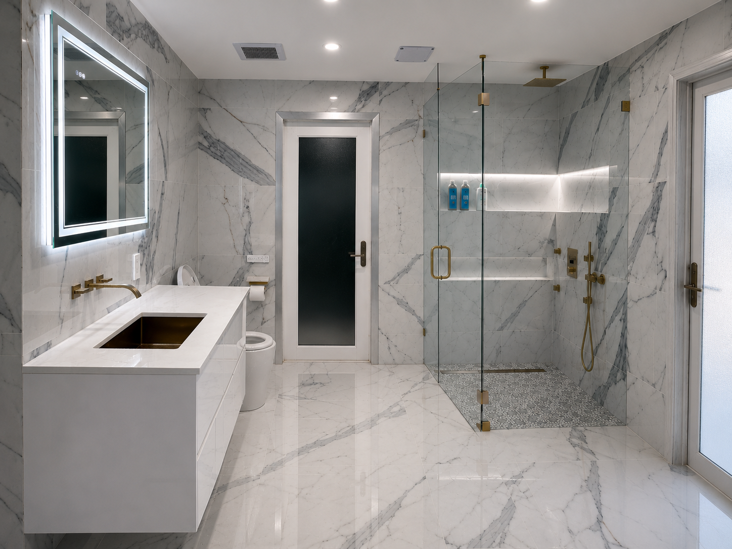 A modern bathroom with marble walls and floor, a rectangular mirror with LED lighting, a white vanity with a copper-colored sink, a toilet, a frosted glass door, and a glass shower enclosure with gold fixtures and built-in shelves.