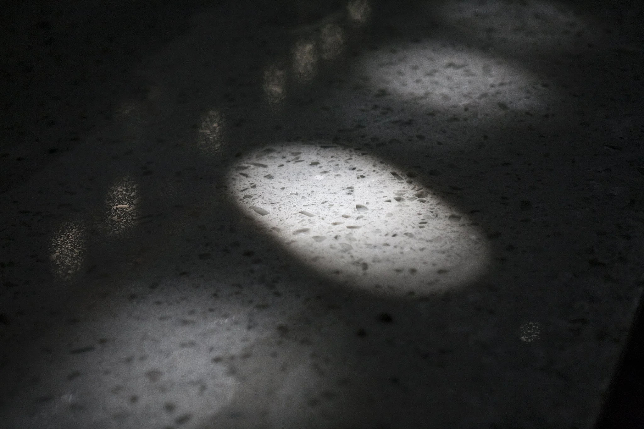 A close-up of a speckled, dark countertop with a bright, oval-shaped spot of light reflecting on it.
