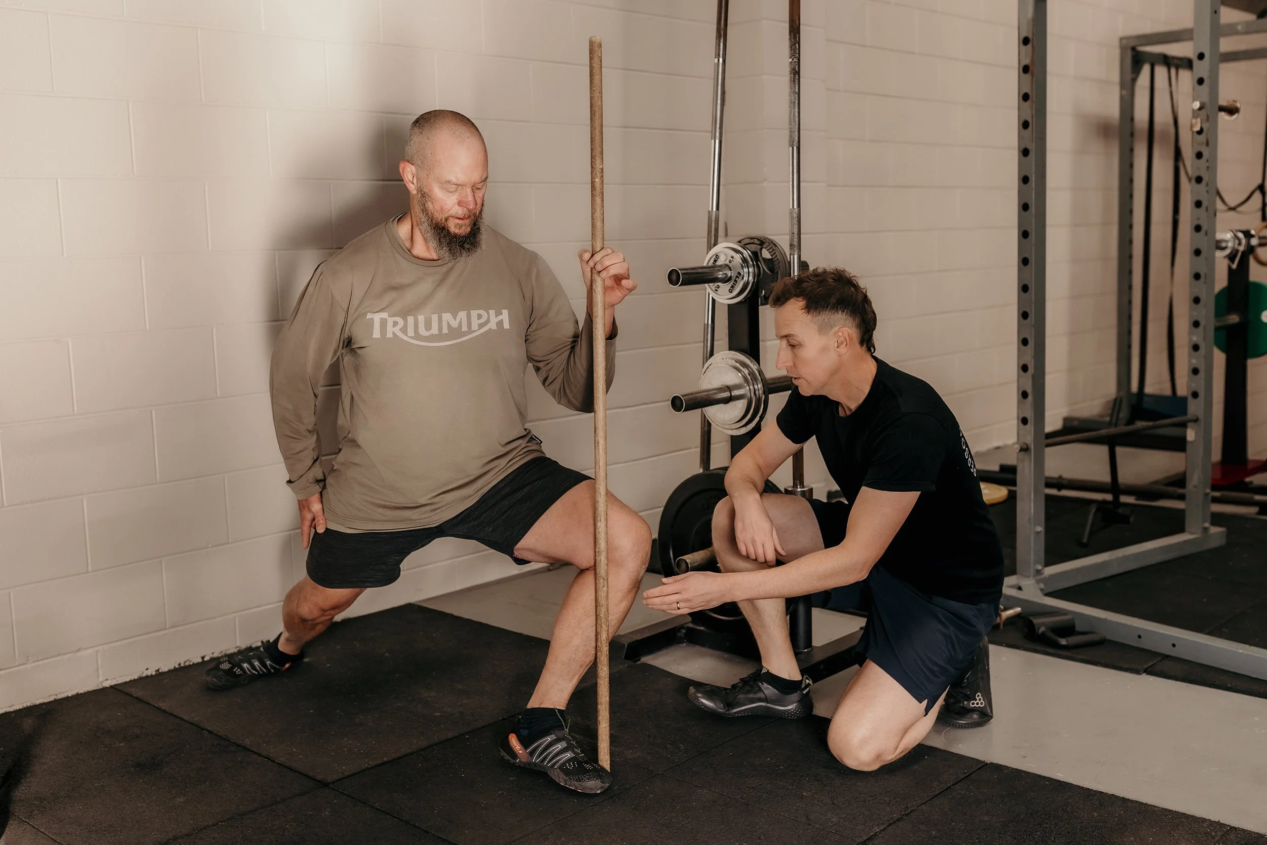 A man lunging in a gym whilst a coach kneels in front of him pointing to his knew