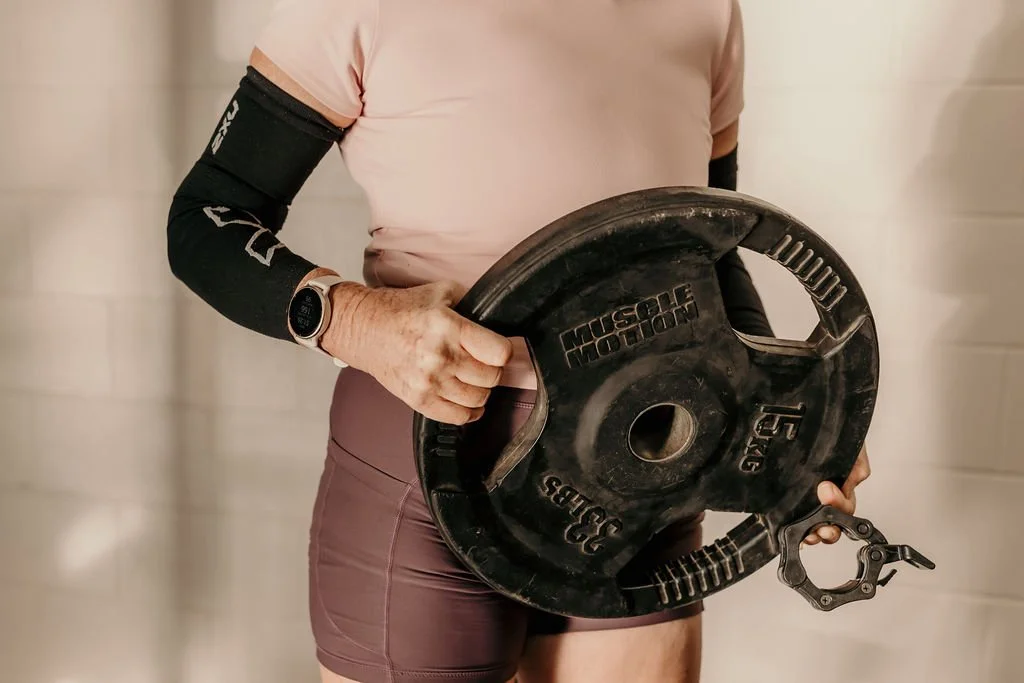 A woman in athletic clothing holding a weight plate with a handle.