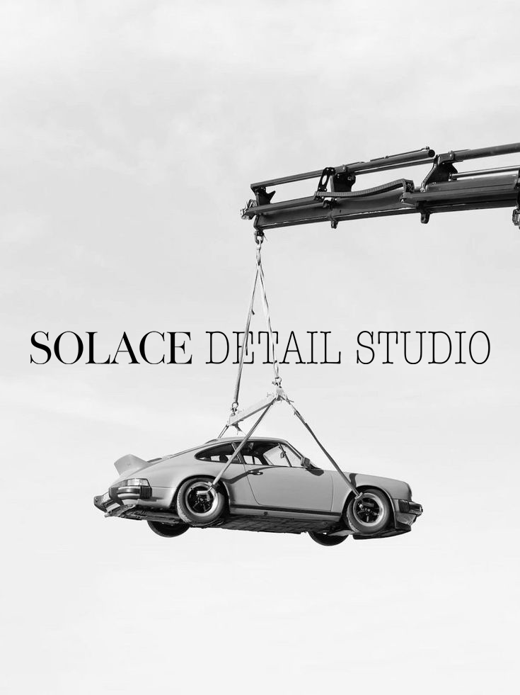 Black and white photo of a crane lifting a classic sports car, with text 'Solace Detail Studio' in the center.