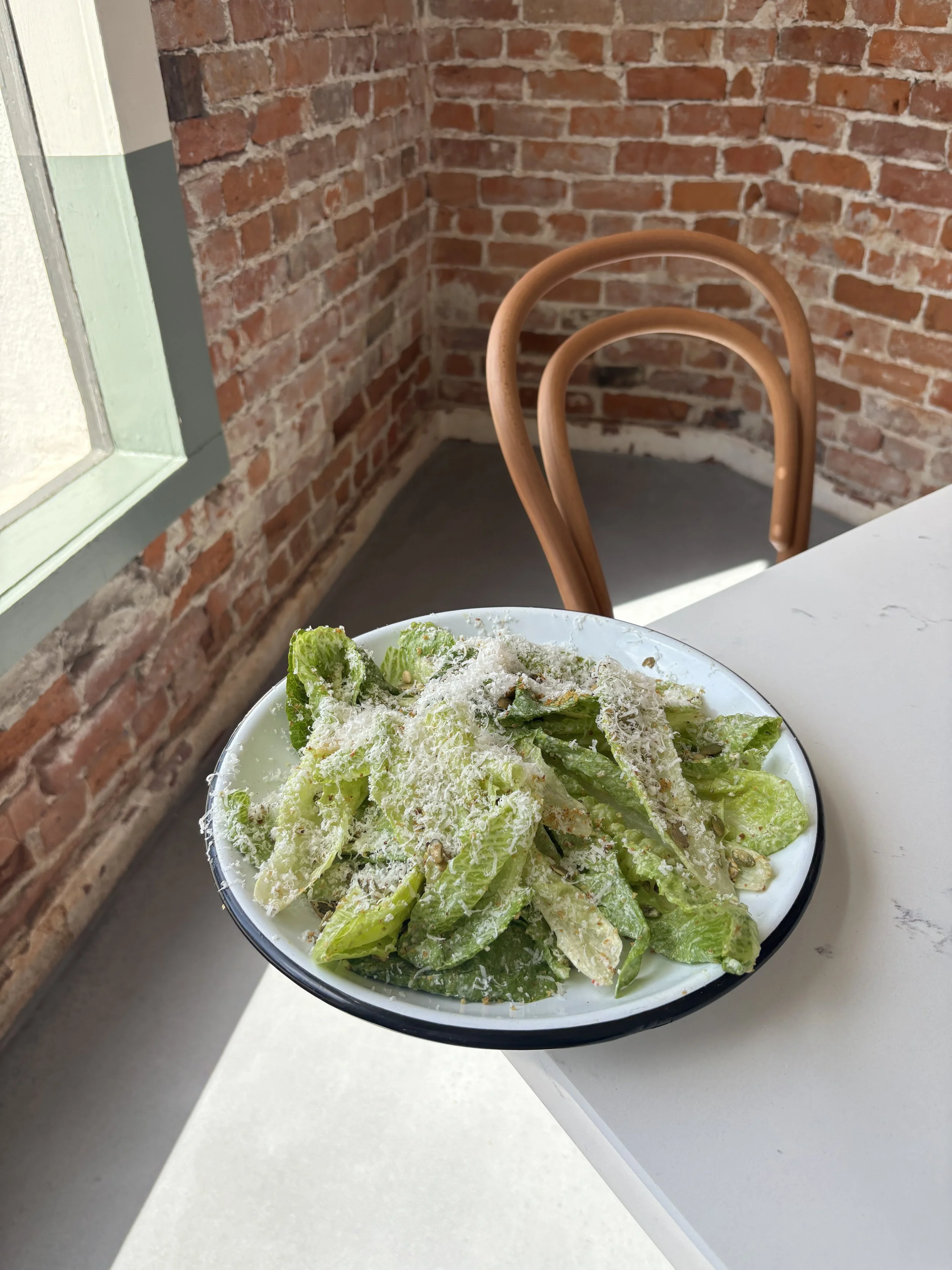 Caesar salad on a white table with exposed brick behind at Mor Mor's Table in Laguna Beach, CA