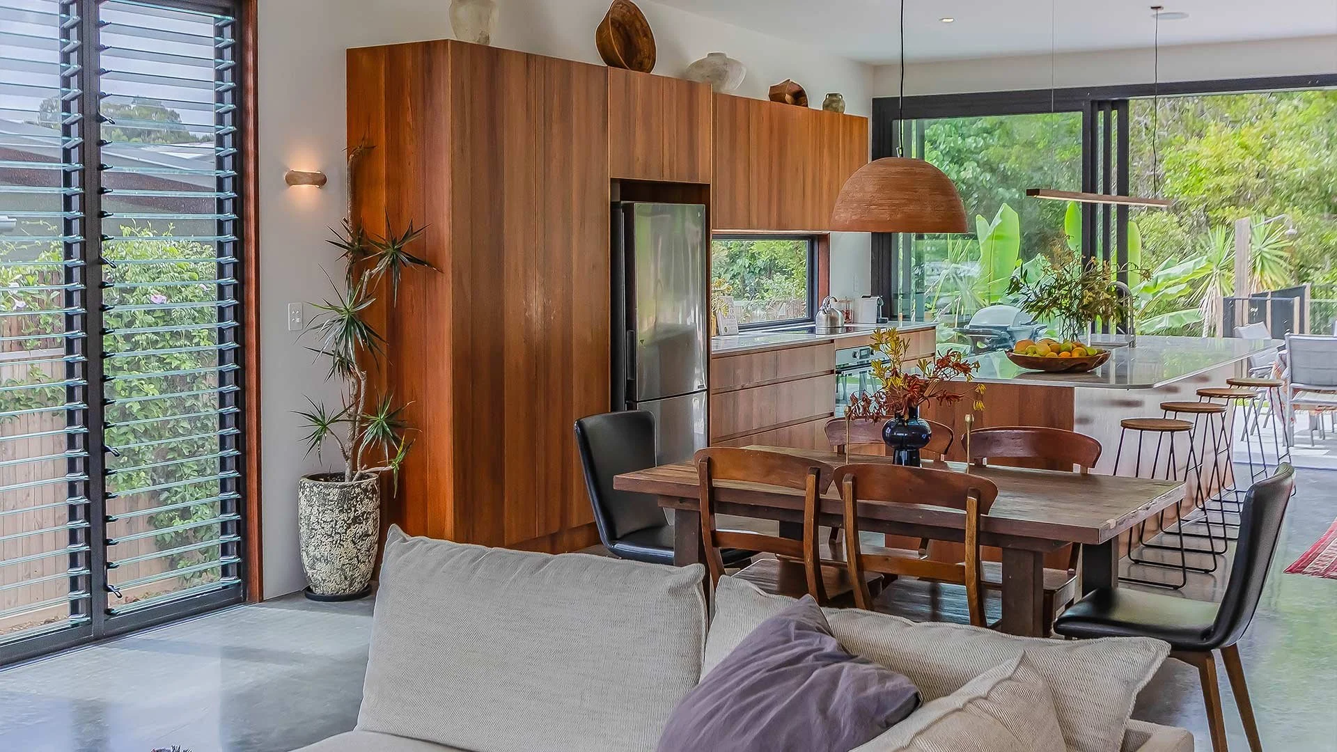 Open-concept kitchen and dining area with large windows, wooden cabinetry, and modern furnishings.