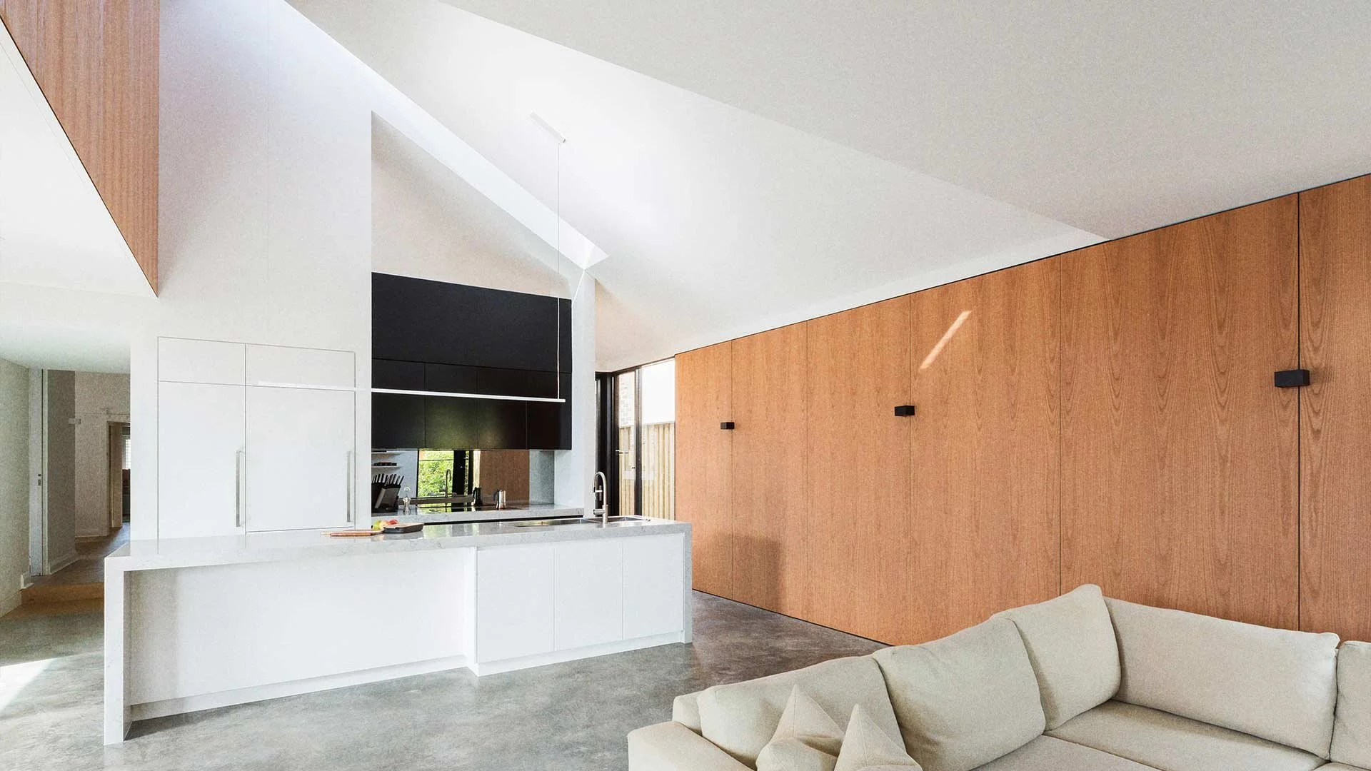 Modern open-concept kitchen with white cabinetry, black and wood accents, and a beige sofa in a living area.