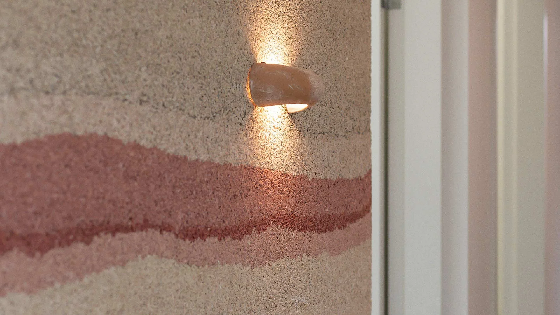 Close-up of a textured wall with a built-in light fixture emitting warm light, with a wavy brown and pink pattern on the wall.
