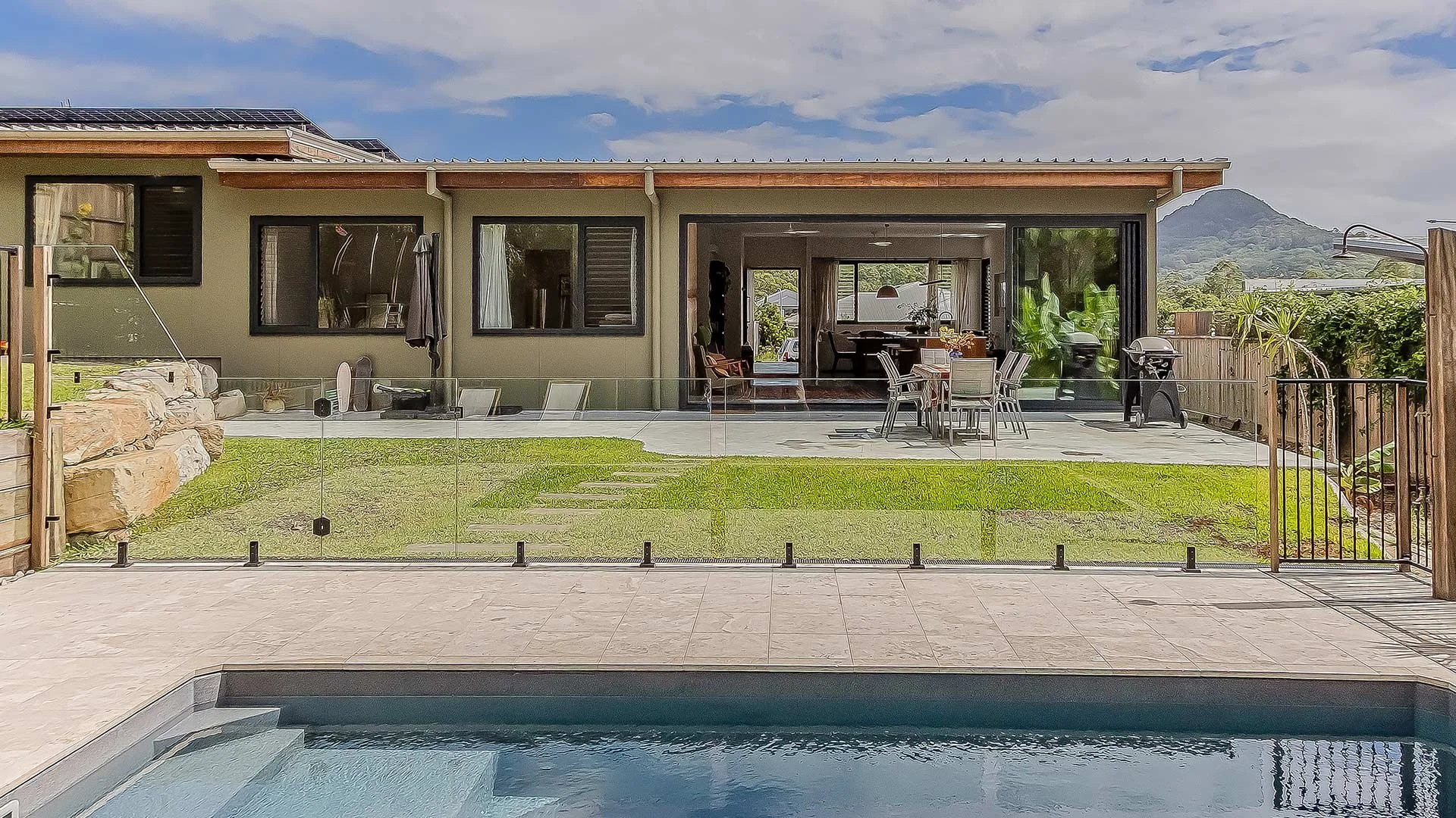 Backyard with swimming pool, patio area, outdoor dining table with chairs, barbecue grill, and a view of mountains in the background.