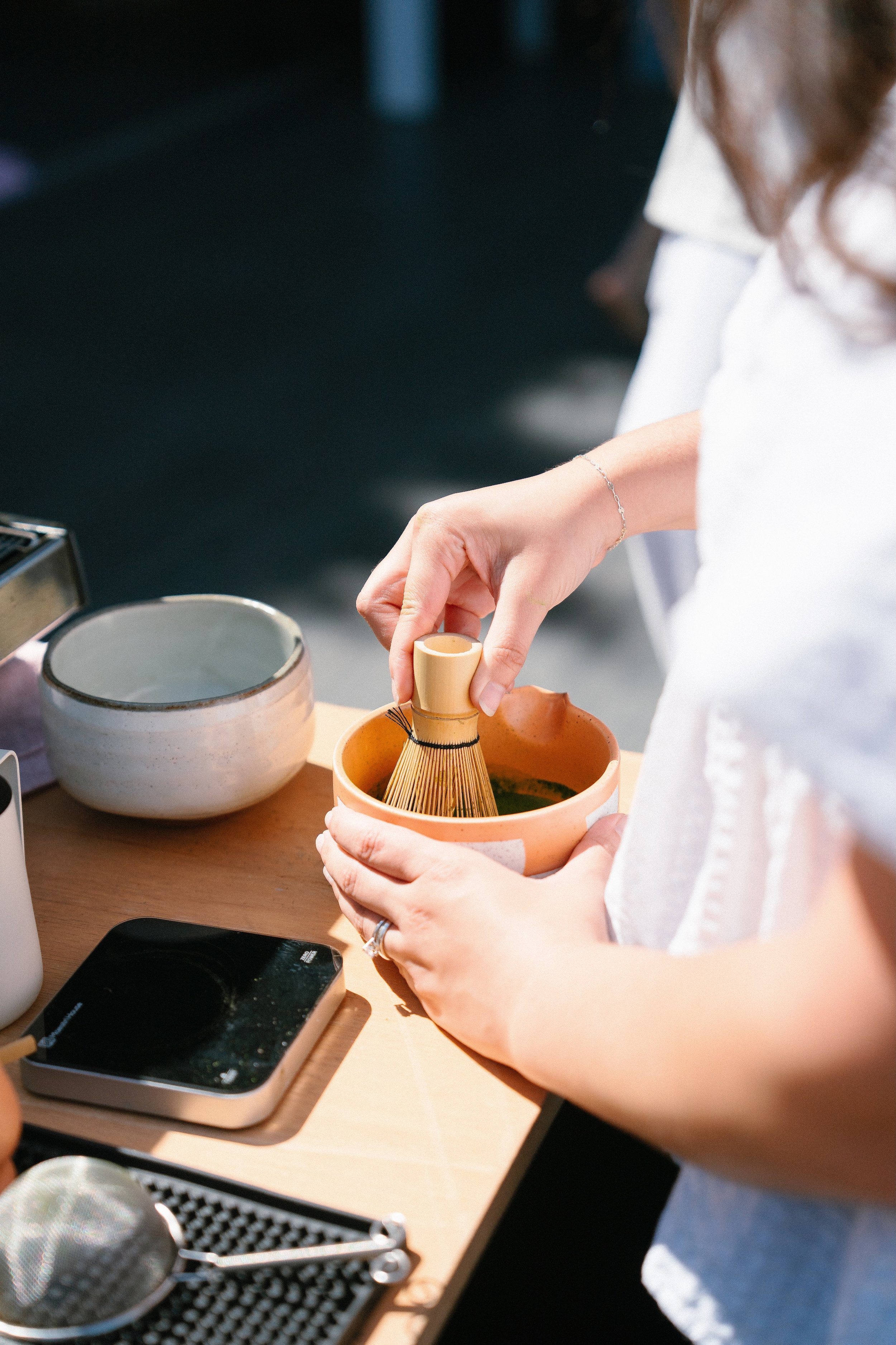woman in white shirt preparing matcha in a checkered bowl, encha matcha, wellness event, private events, malibu coffee catering, hollywood hills matcha bar, dana point, huntington beach, laguna beach, laguna hills, huntington beach, costa mesa, lid