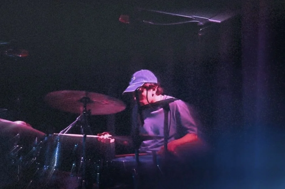 A person wearing a baseball cap playing drums in a dimly lit setting.