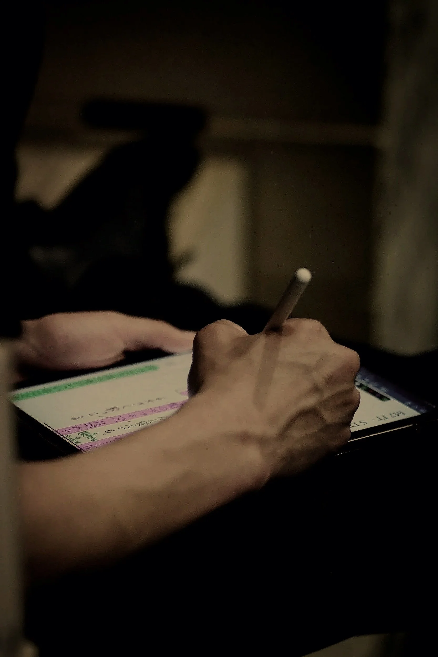 A person writing notes for content planning on a piece of paper with a pencil, in a dimly lit environment.