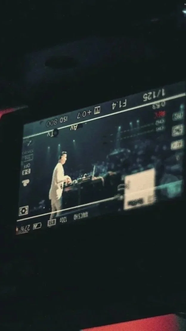 View of a person performing as a guitaris in a music video or live music event, seen through a camera's screen display during a concert or event at night.