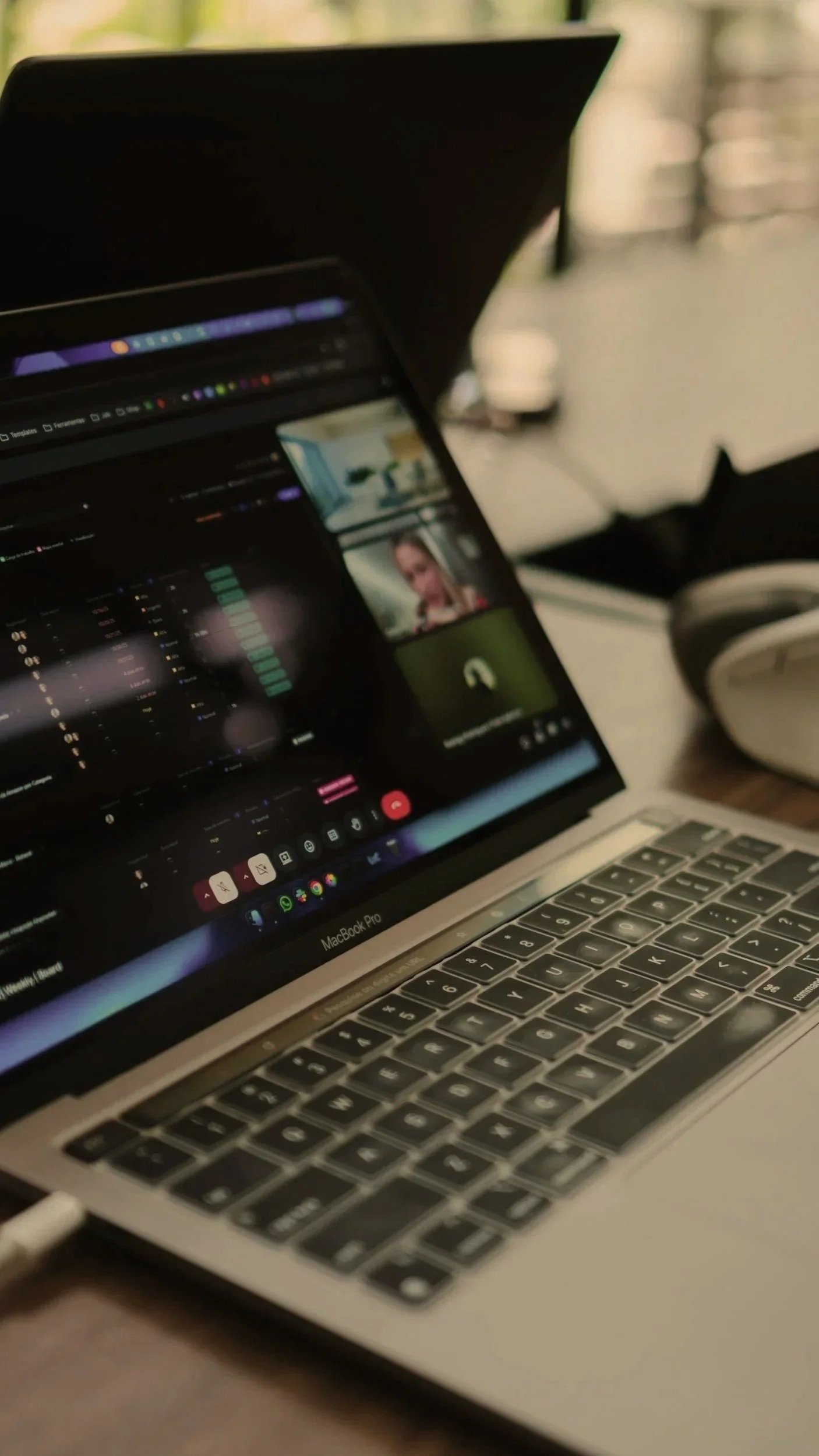 Close-up of a MacBook Pro laptop on a desk, with a video call and audio mixing software open on the screen. A pair of over-ear headphones is visible to the right.