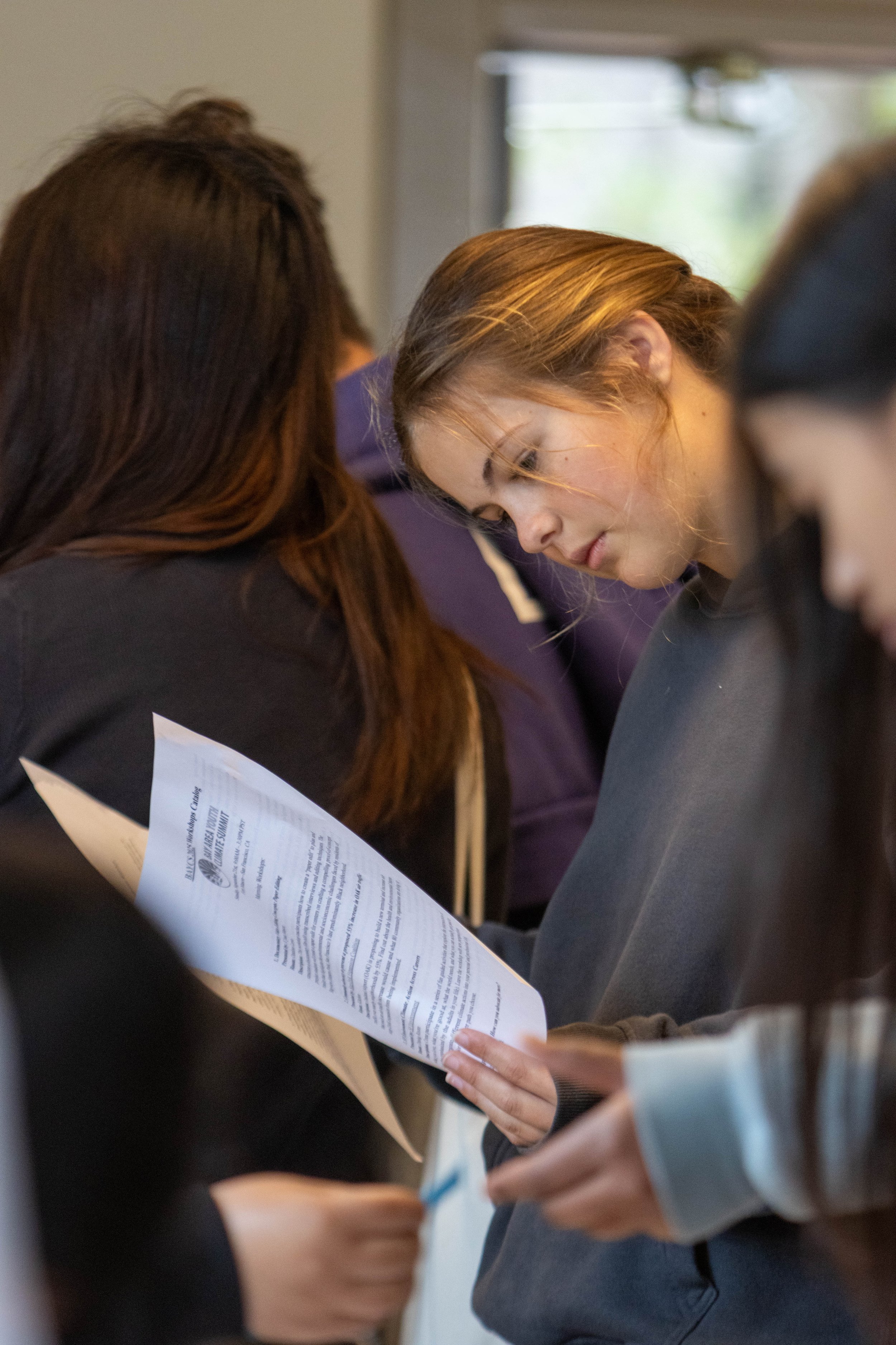 Two women looking at a sheet of paper or brochure together in a crowded indoor setting.