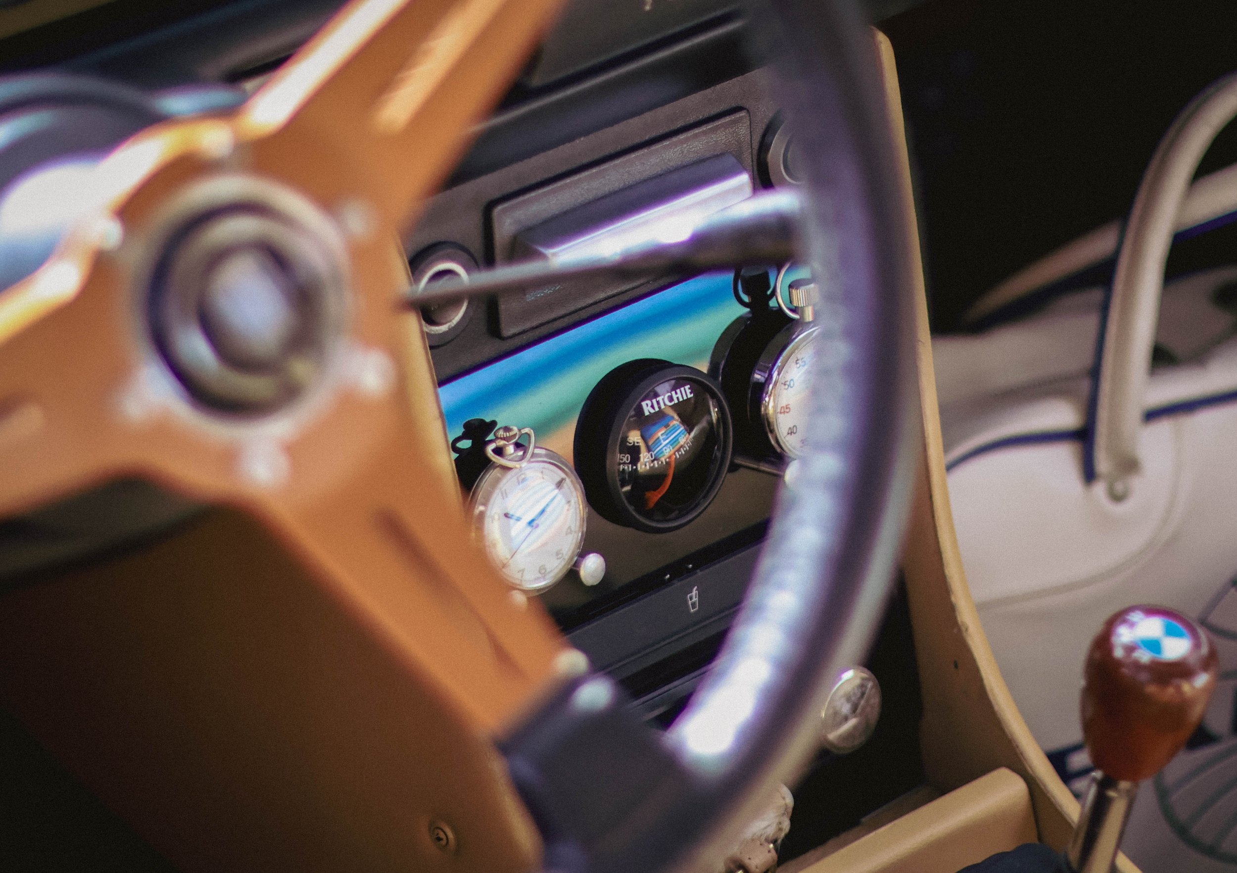 Close-up of a vintage car dashboard with various dials and switches, including an analog clock, temperature gauge, and radio, with a person's finger pointing towards the dashboard.