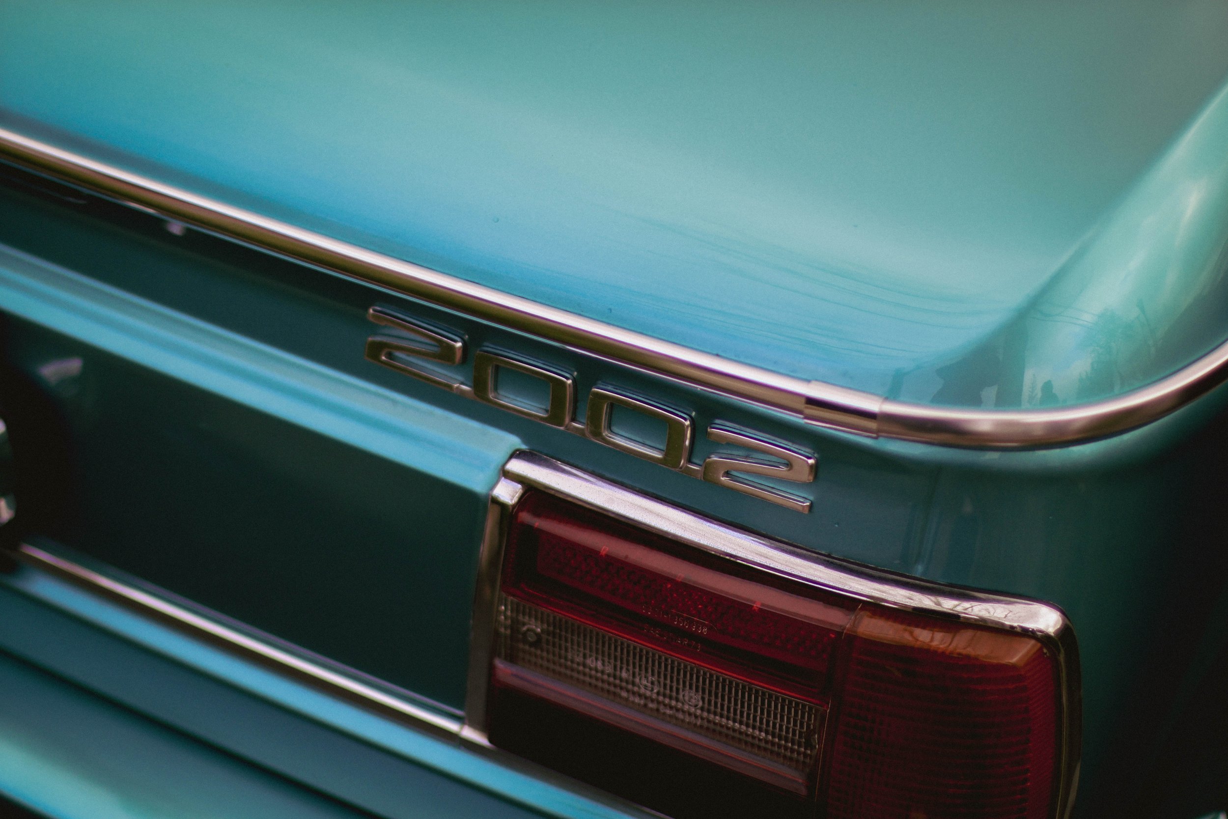 Close-up photo of the rear end of a vintage green car, showing the tail light and the badge with the number '3000'.
