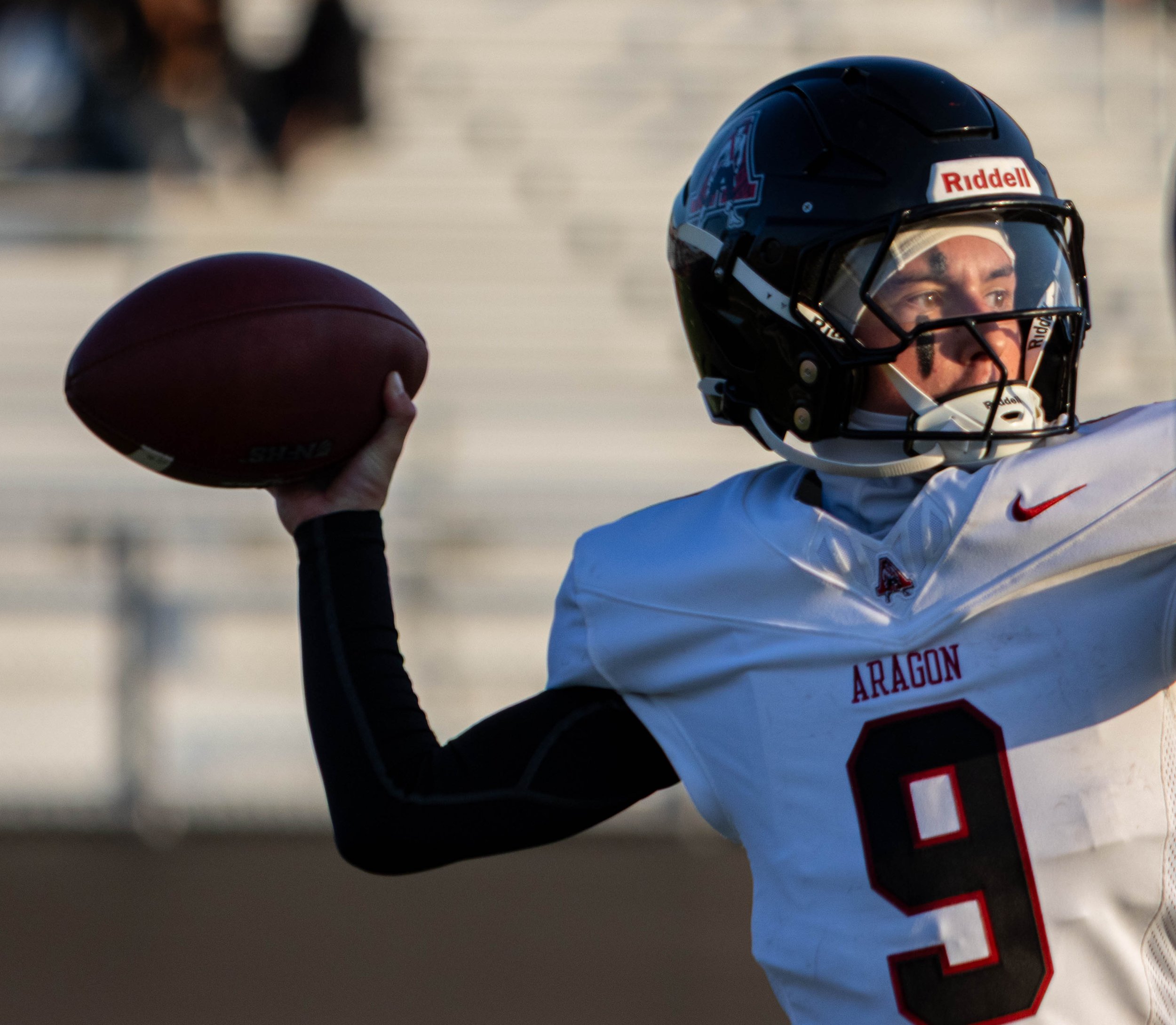 A football player in a white uniform with red and black accents, wearing a helmet, prepares to throw a football on the field.