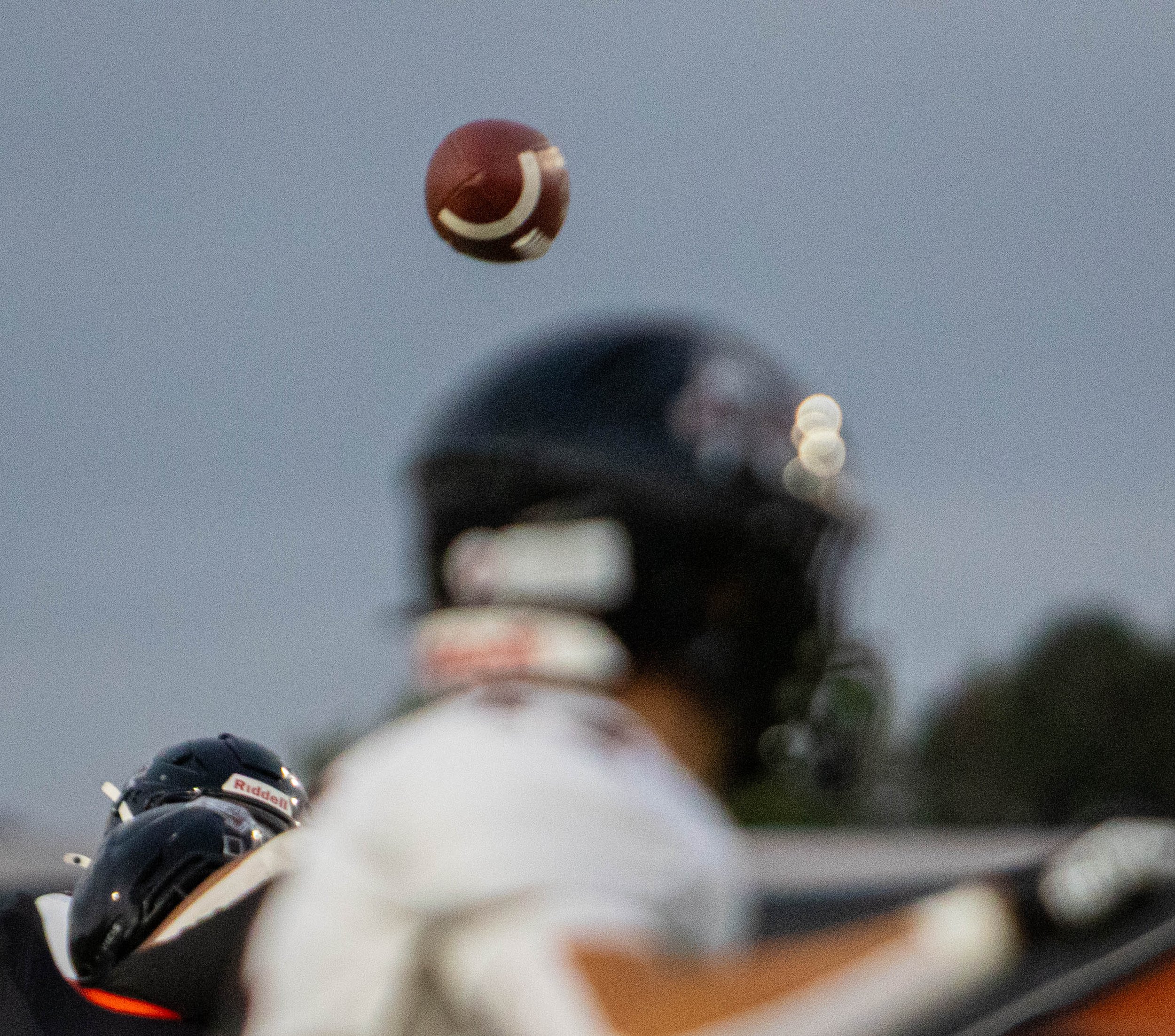 Line of ice hockey players in black jerseys with helmets, viewed from behind, with a football flying through the sky.