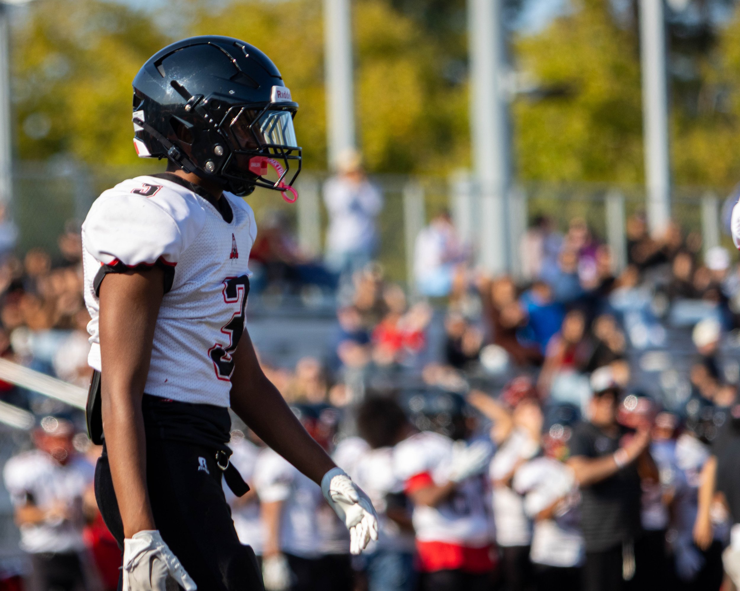 A football player in a black helmet and white jersey standing on a field during a game with a crowd in the background.