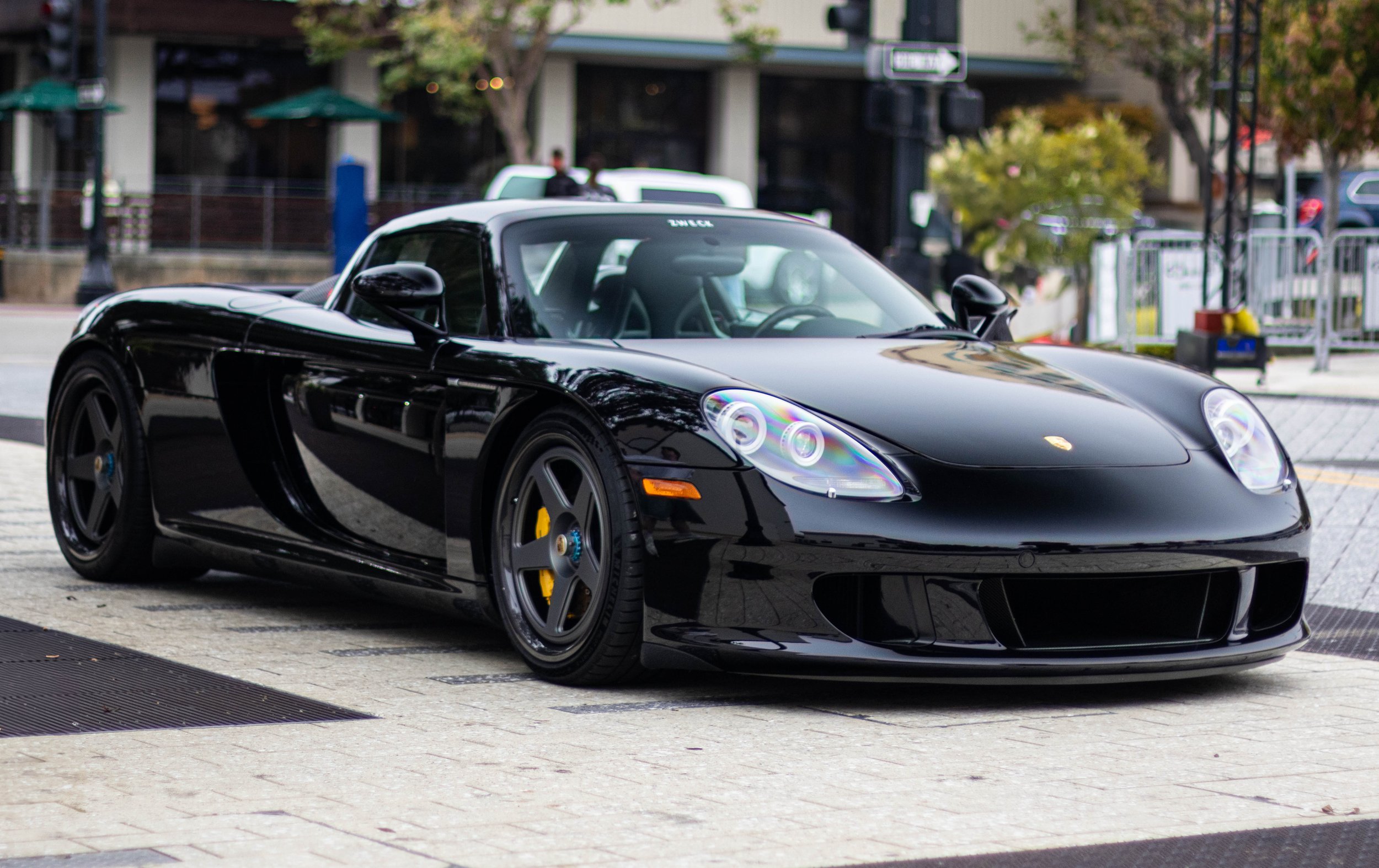 A black Porsche sports car parked on a city street, with trees and buildings in the background.