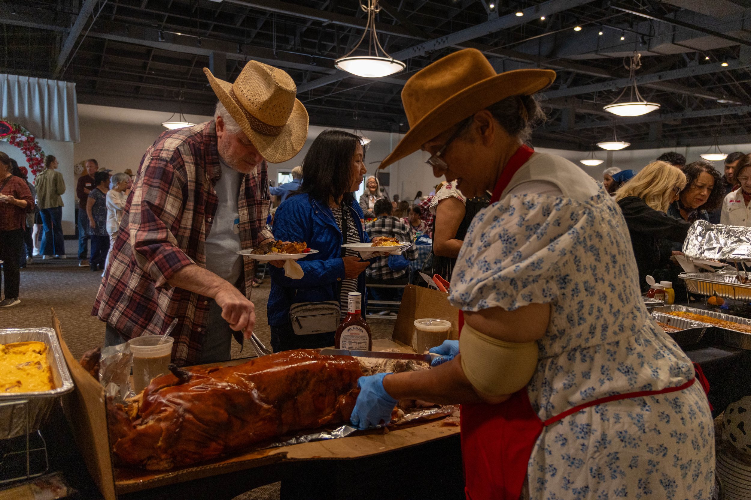 People at a buffet table serving food at a gathering or event, with plates and food items in focus.