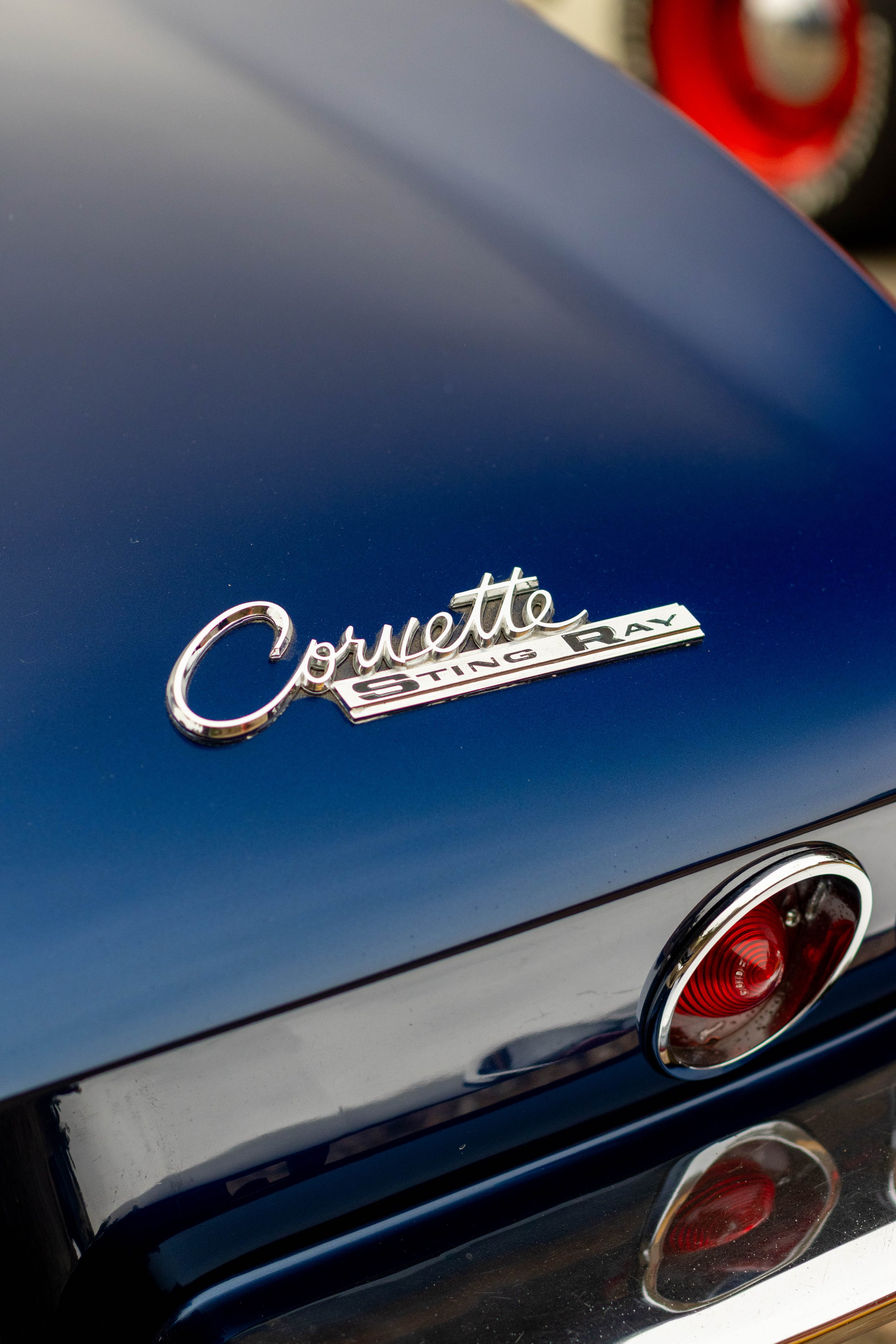 Close-up of a Chevrolet Corvette emblem on the back of a blue sports car, with red taillights visible.