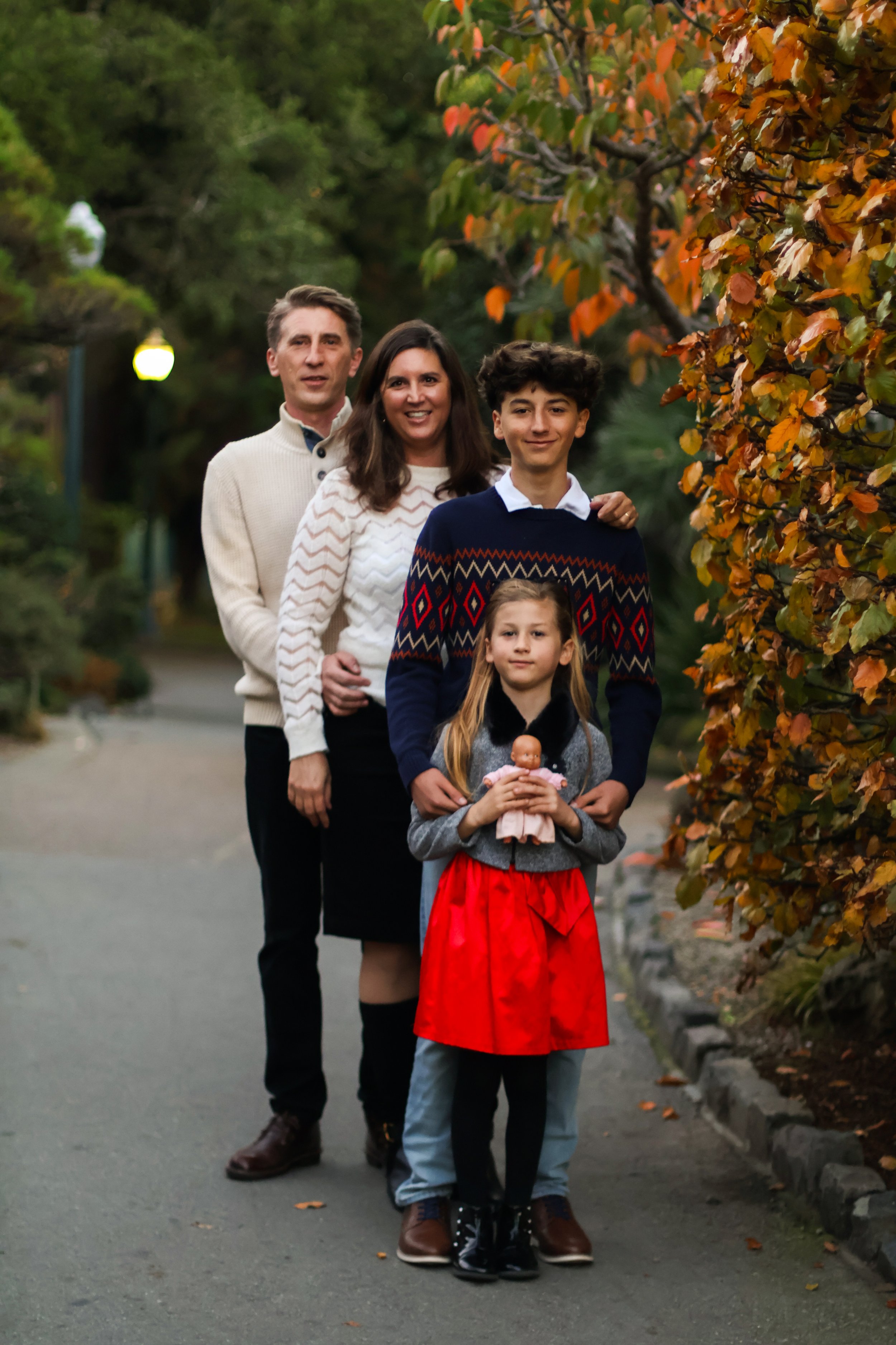 Family of five walking on a path surrounded by autumn trees, with three adults and two children; the young girl holds a doll.