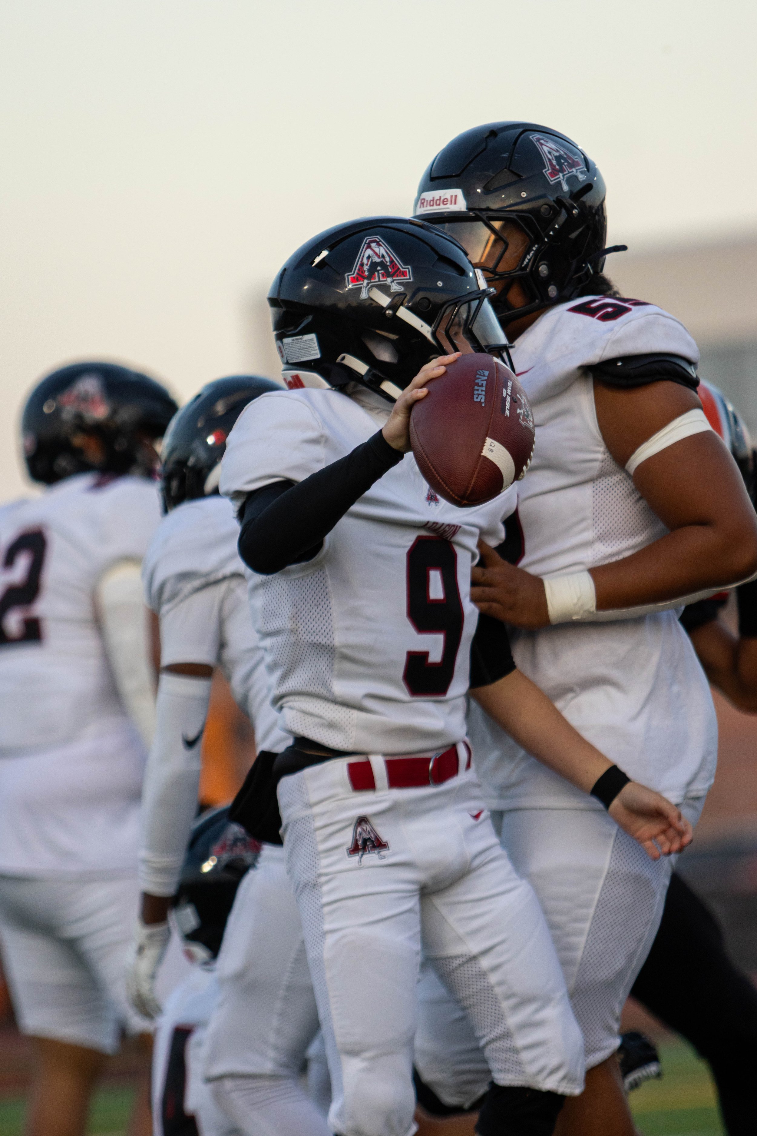 American football players in black helmets and white uniforms celebrating on the field, with one player holding a football.