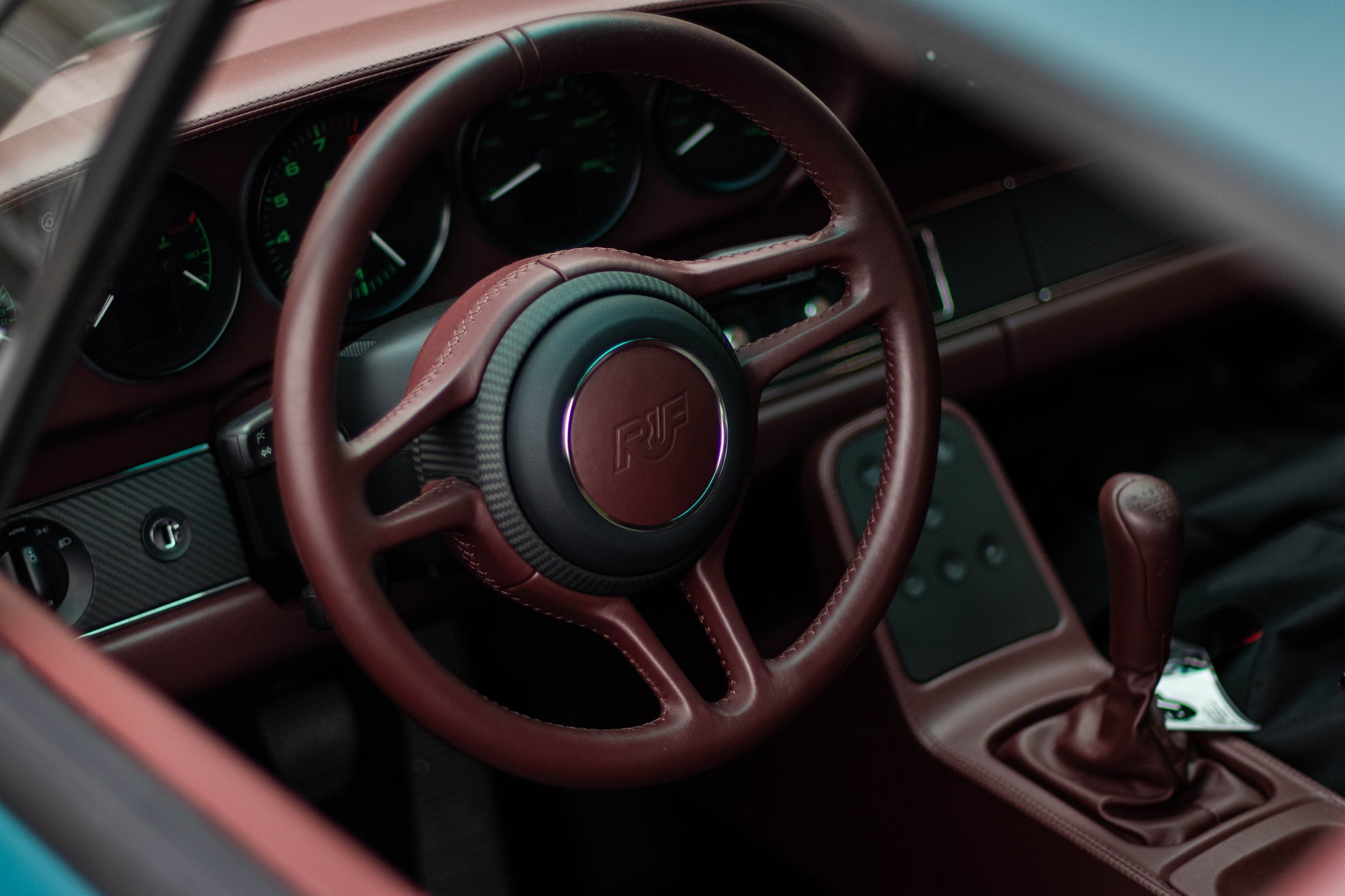 Close-up of a car interior dashboard with a maroon leather-wrapped steering wheel and gauges with green needles.