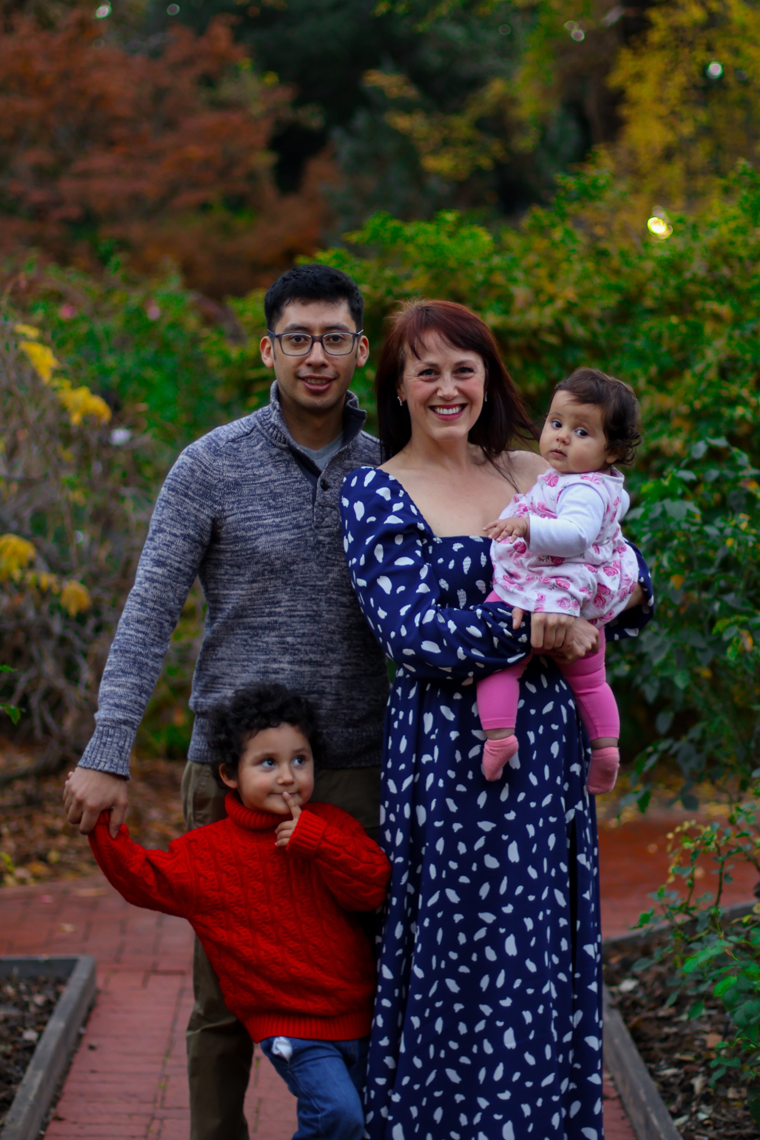 A family portrait outdoors with two adults and two children, surrounded by autumn foliage.