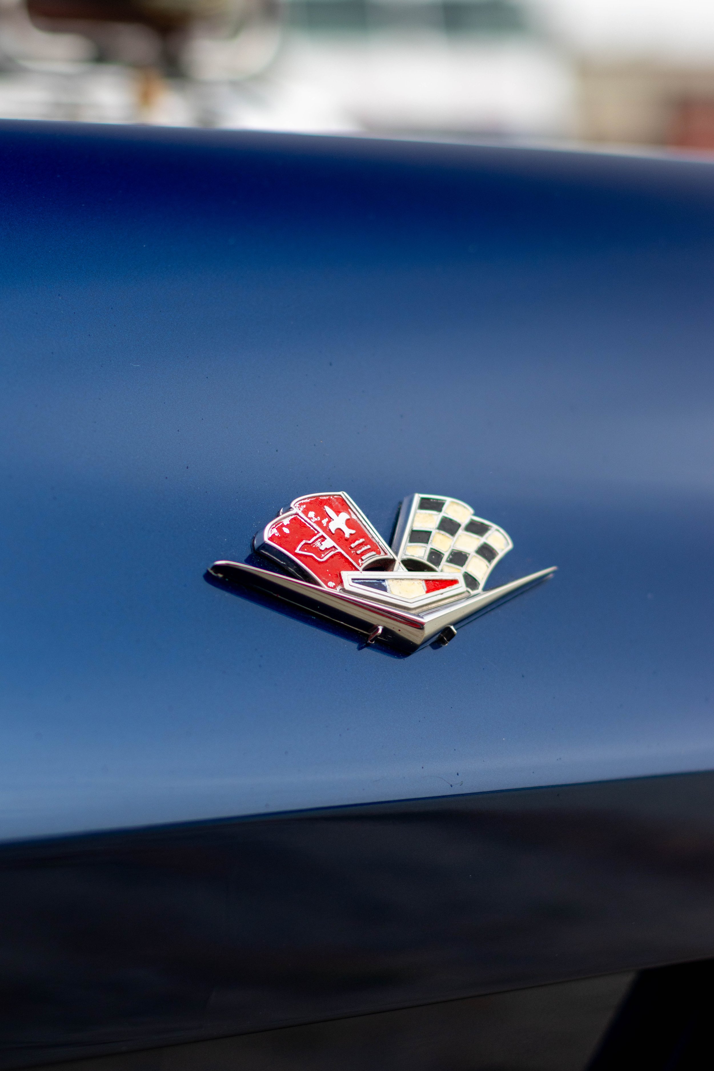 Close-up of a vintage car emblem featuring a checkered flag and a red shield with a white logo, mounted on a dark blue car body.
