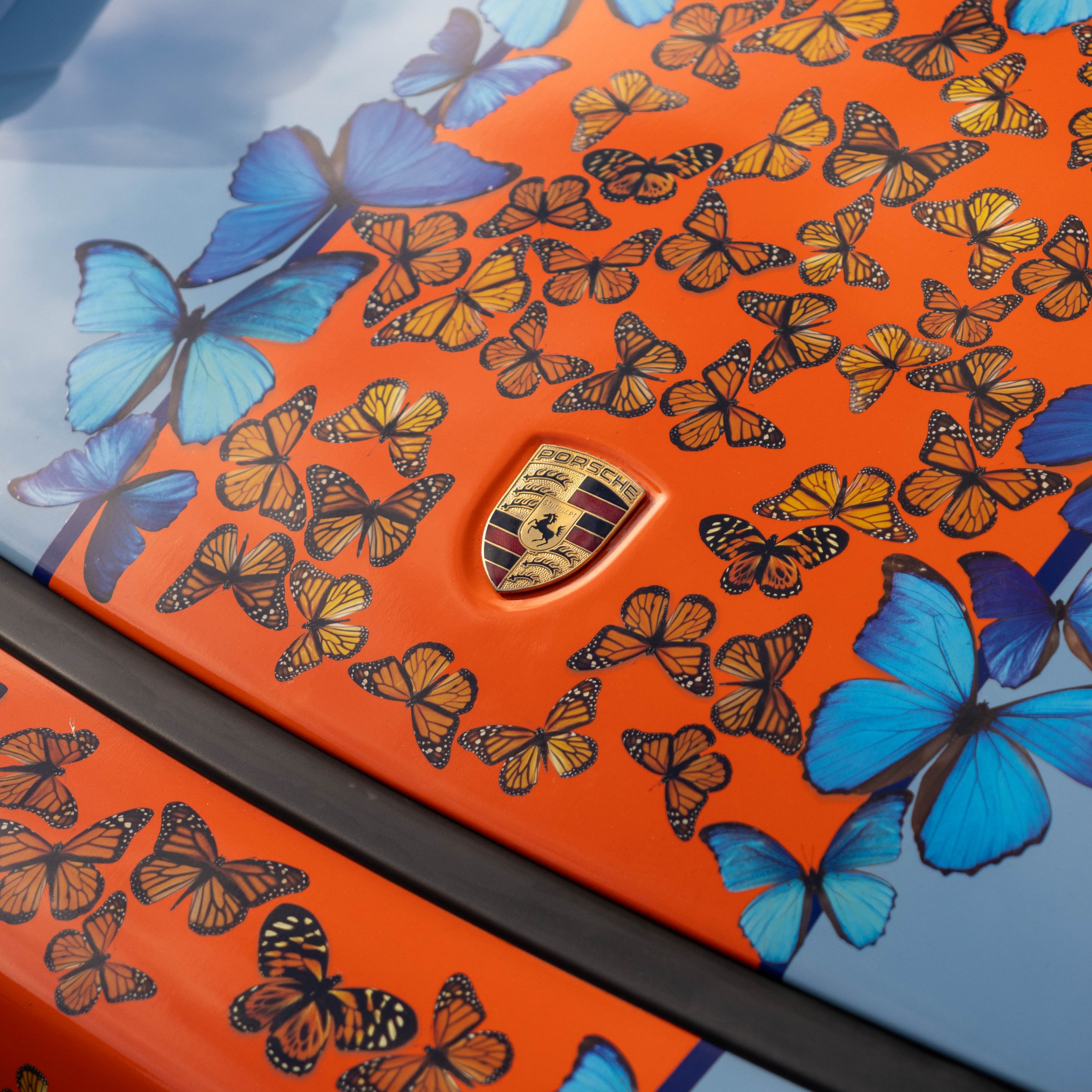 Orange surface decorated with numerous monarch butterfly stickers and a Porsche emblem.