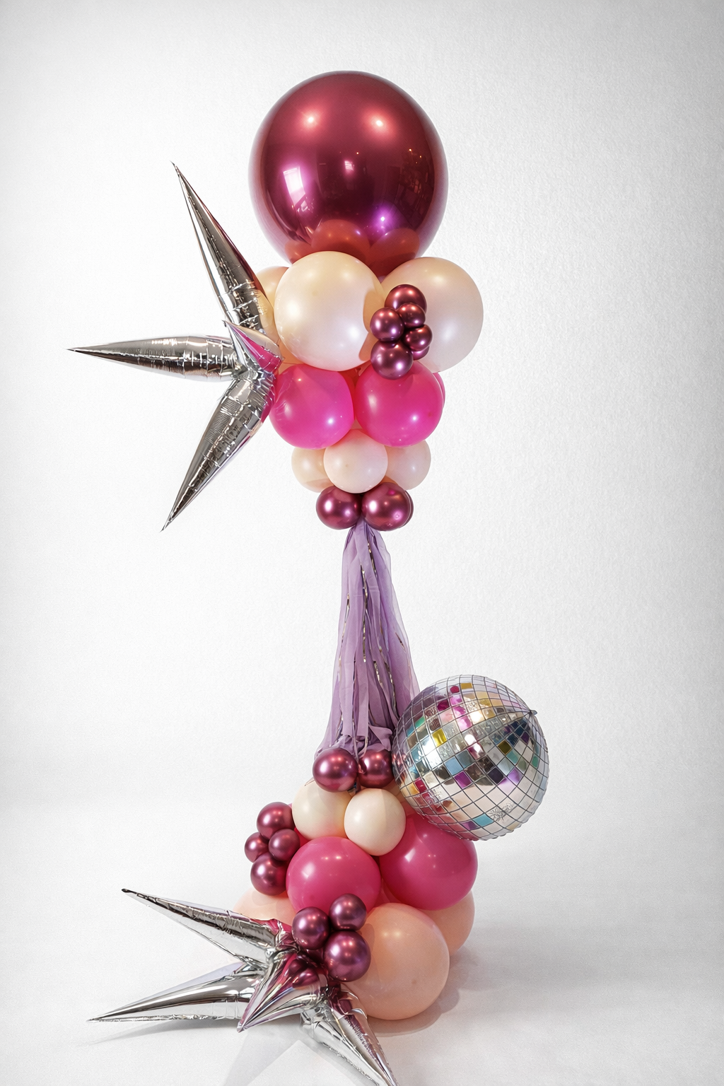 Balloon arrangement with pink, white, and purple balloons, silver star-shaped balloons, a disco ball, and purple streamers.
