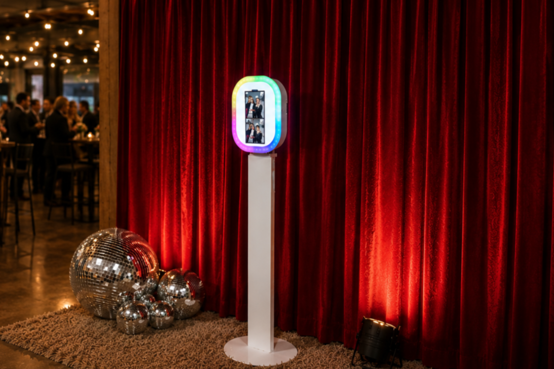 Digital photo booth setup with red velvet backdrop, neon lights, and giant mirror balls for an event in Boston.