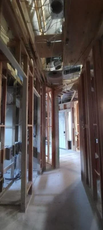 Construction site with exposed wooden framing and plumbing, electrical wiring, and HVAC ductwork in a hallway.