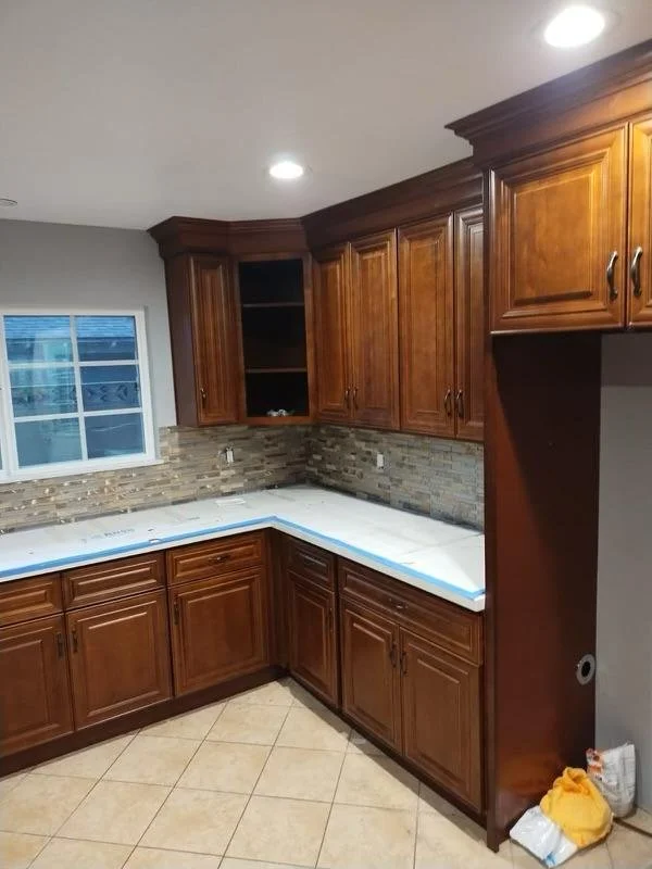 Kitchen with wooden cabinets, a window, and a tiled backsplash, showing construction or renovation in progress.