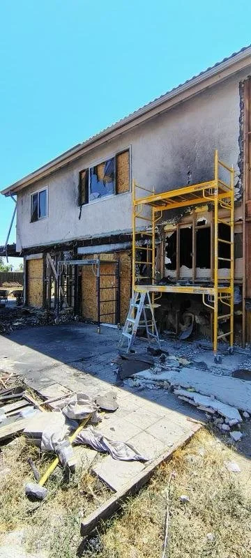 Burned out house with damaged walls, broken windows, and a yellow scaffolding in front.