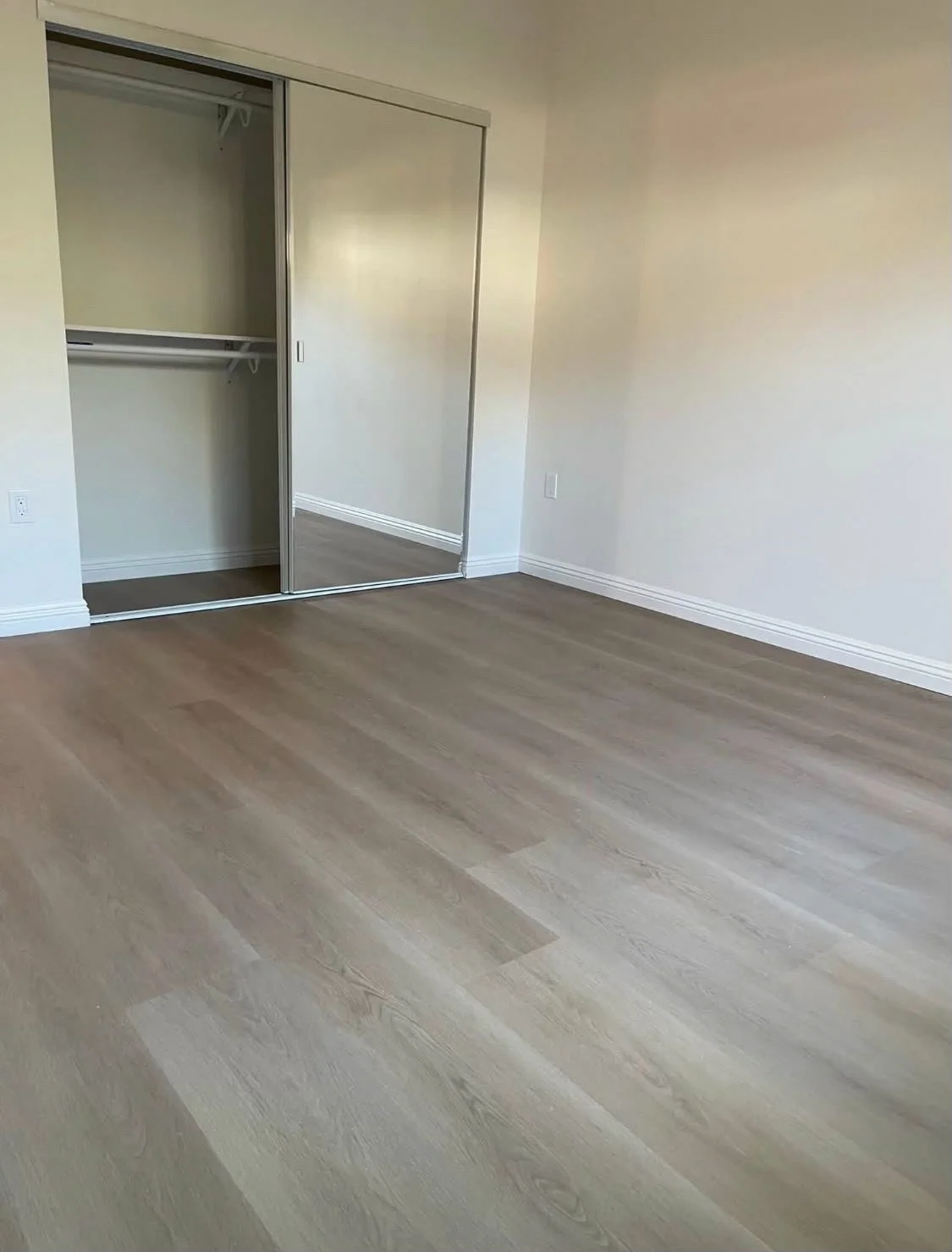Empty room with wood flooring, white walls, and a closet with sliding mirror doors.