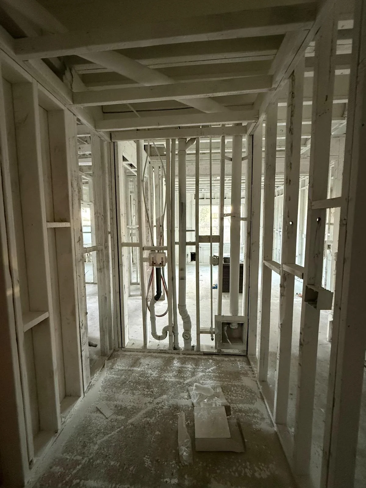 Interior view of a house under construction showing exposed framing, plumbing, and electrical components without drywall or finishes.
