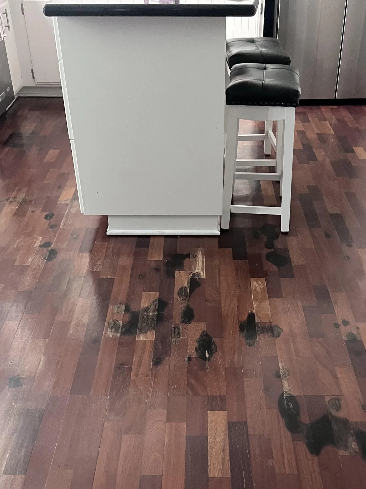 A kitchen island with a white base and black seating area, positioned on a dark wooden floor with visible black stains.