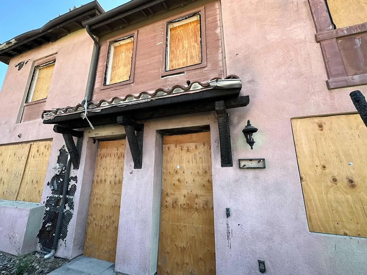 A house with boarded-up windows and doors, some damage to the exterior, and missing or broken fixtures.