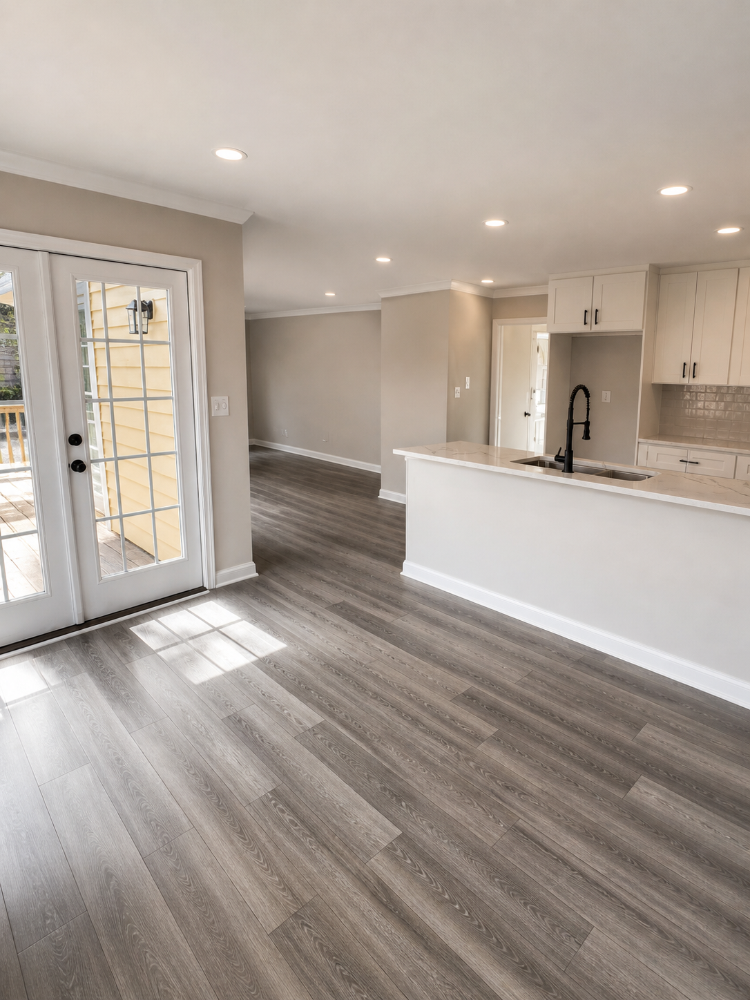 Empty modern kitchen and living space with wood flooring, white cabinets, and a sliding glass door leading to a patio.