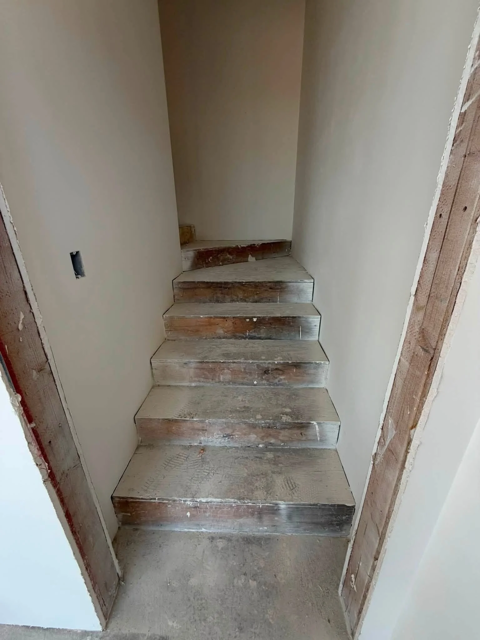 Unfinished wooden staircase leading to a small, enclosed upper level with bare walls and an electrical outlet on the left side.