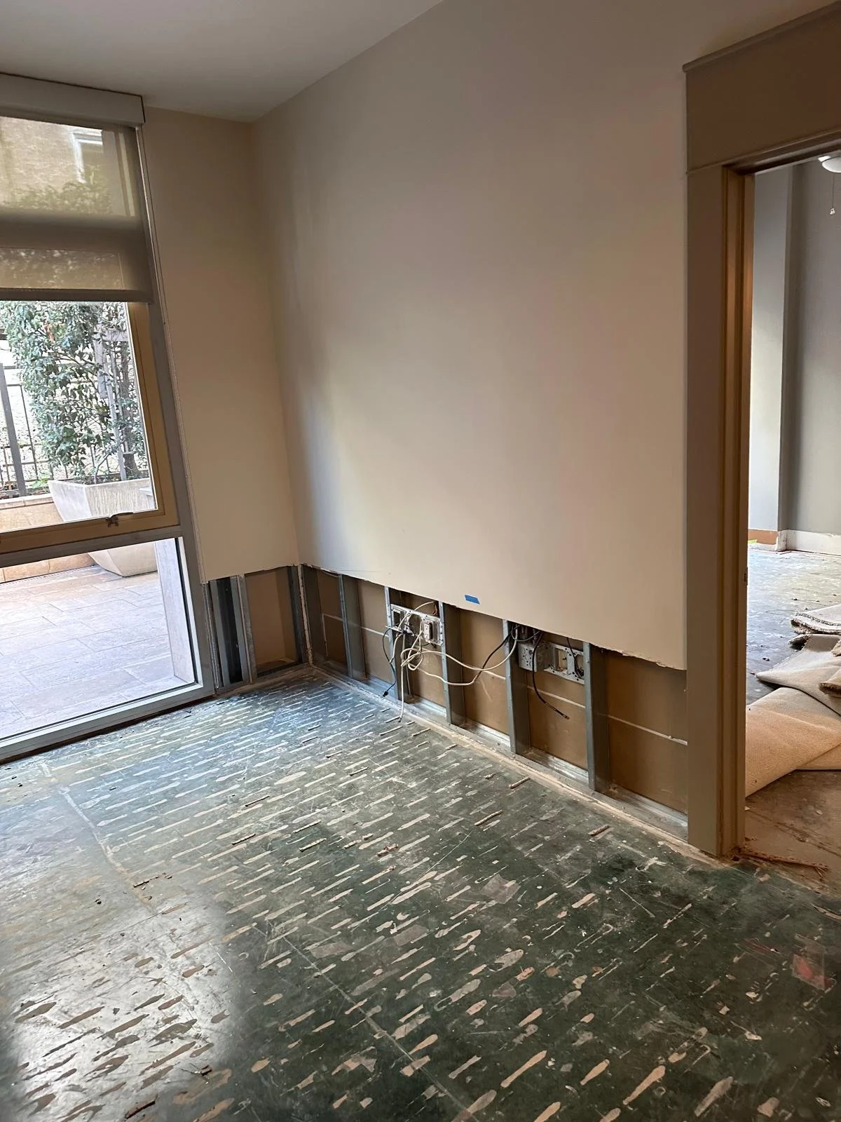 Living room undergoing renovation with exposed electrical wiring and removed baseboards, next to a sliding glass door leading to an outdoor patio.