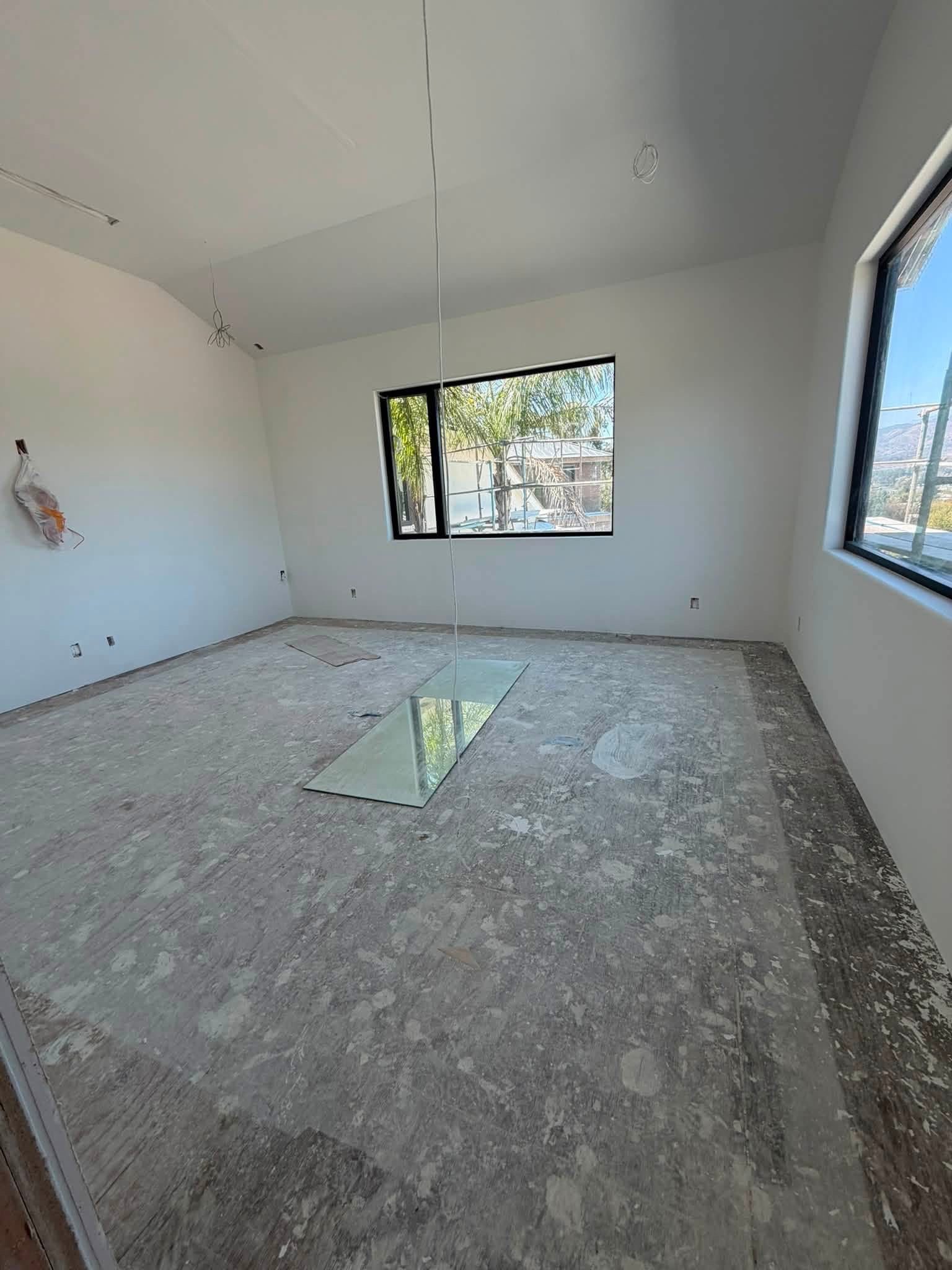 Empty room under construction with two windows, unfinished flooring, and exposed wires on the ceiling.