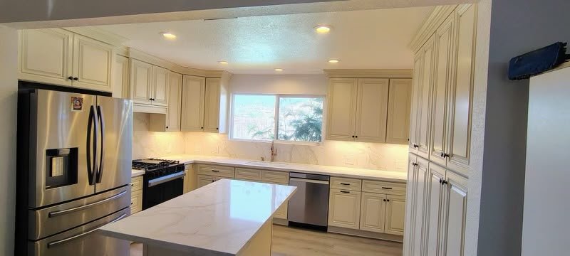 Modern kitchen with white cabinets, stainless steel refrigerator, stove, dishwasher, central island, and large window.