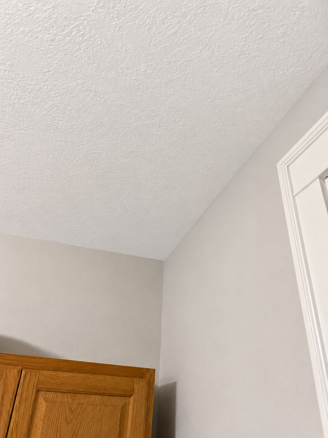 The ceiling, wall, corner of a room, and part of a wooden cabinet with a white door frame.