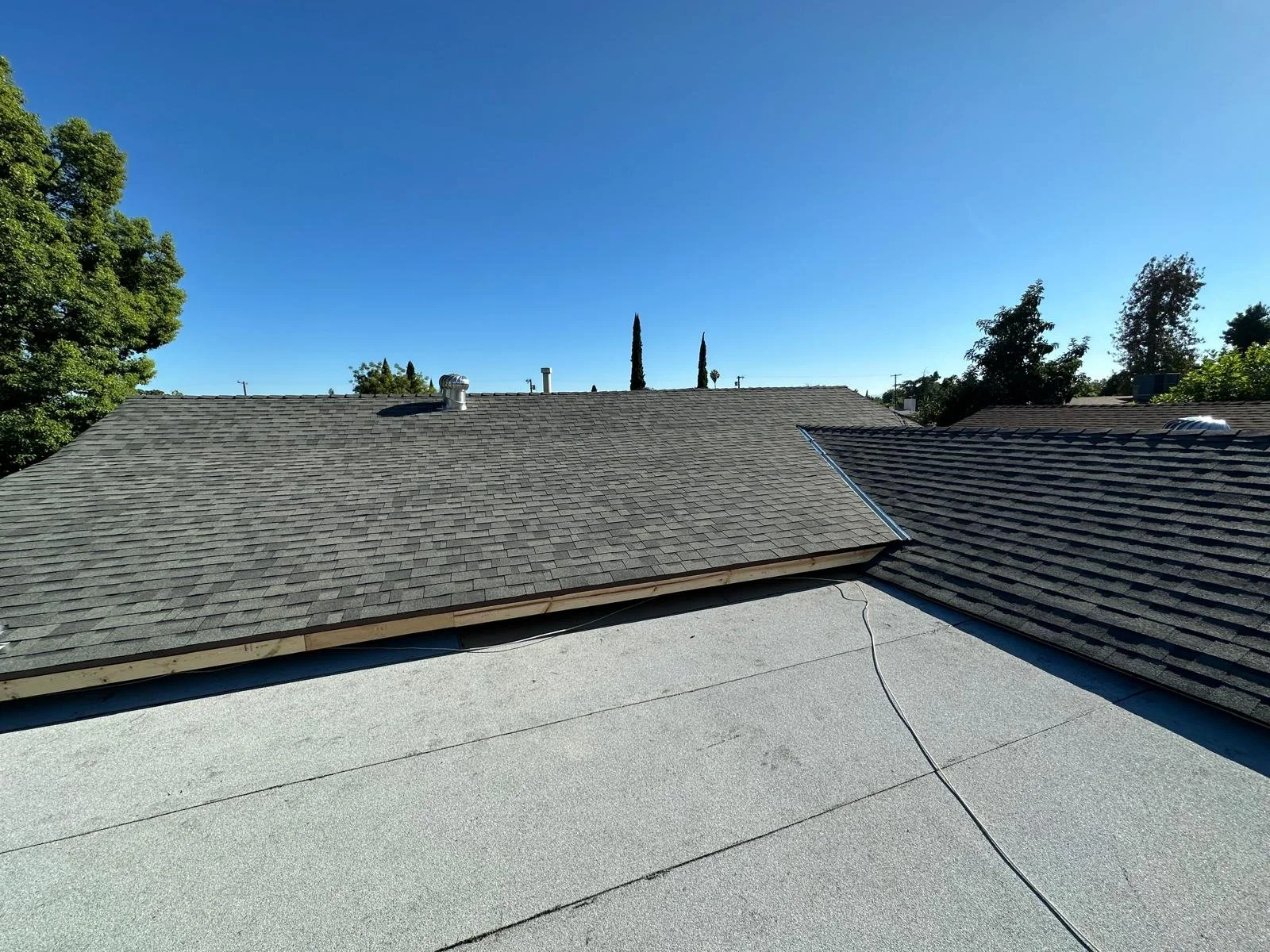 View of rooftops with shingle roofs and a clear blue sky, trees in the background.
